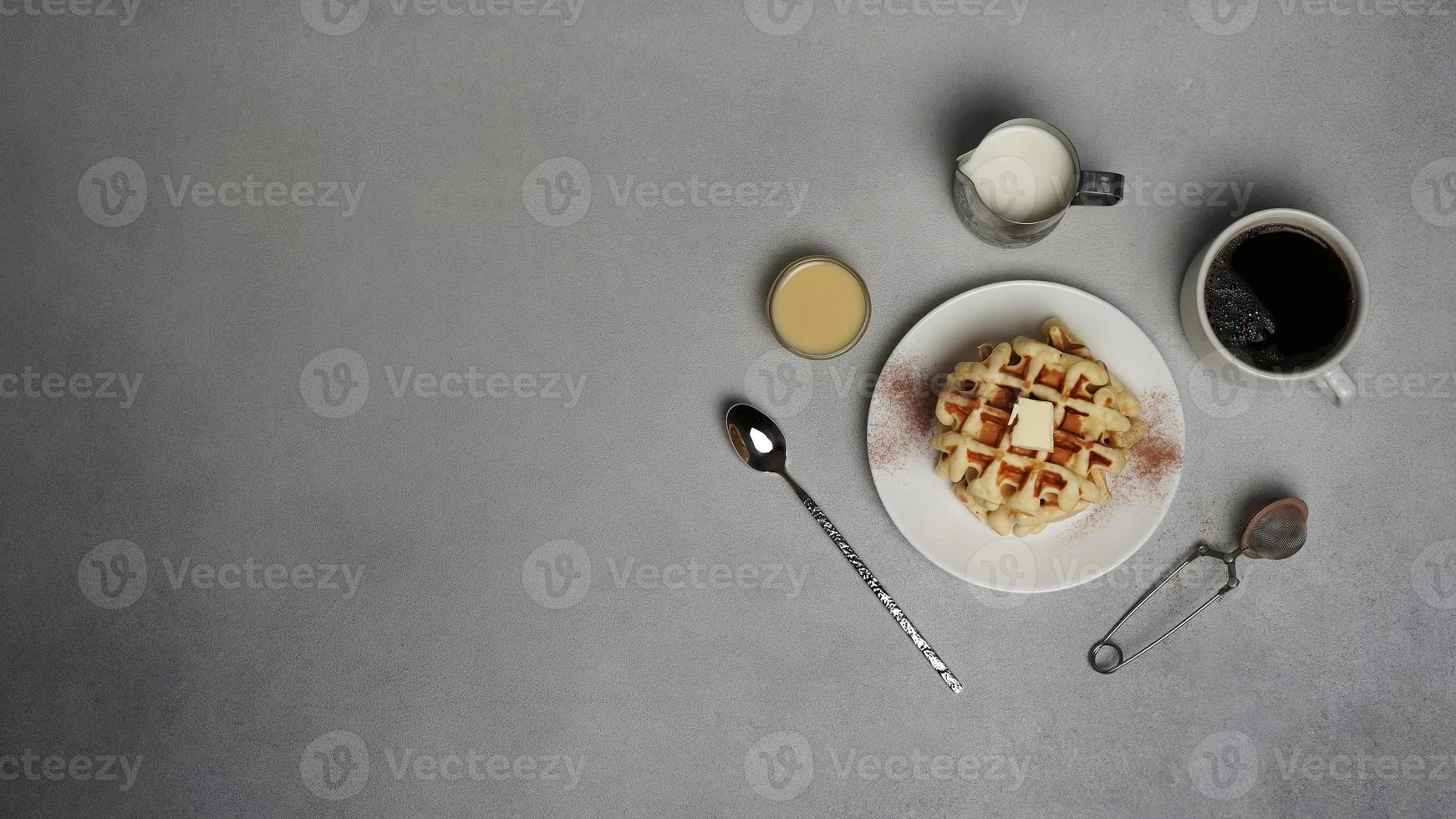 superiore Visualizza di gustoso cialde piatto, caramello salsa, caffè tazza, latte, cucchiaio da dessert, filtro su un' grigio calcestruzzo sfondo foto