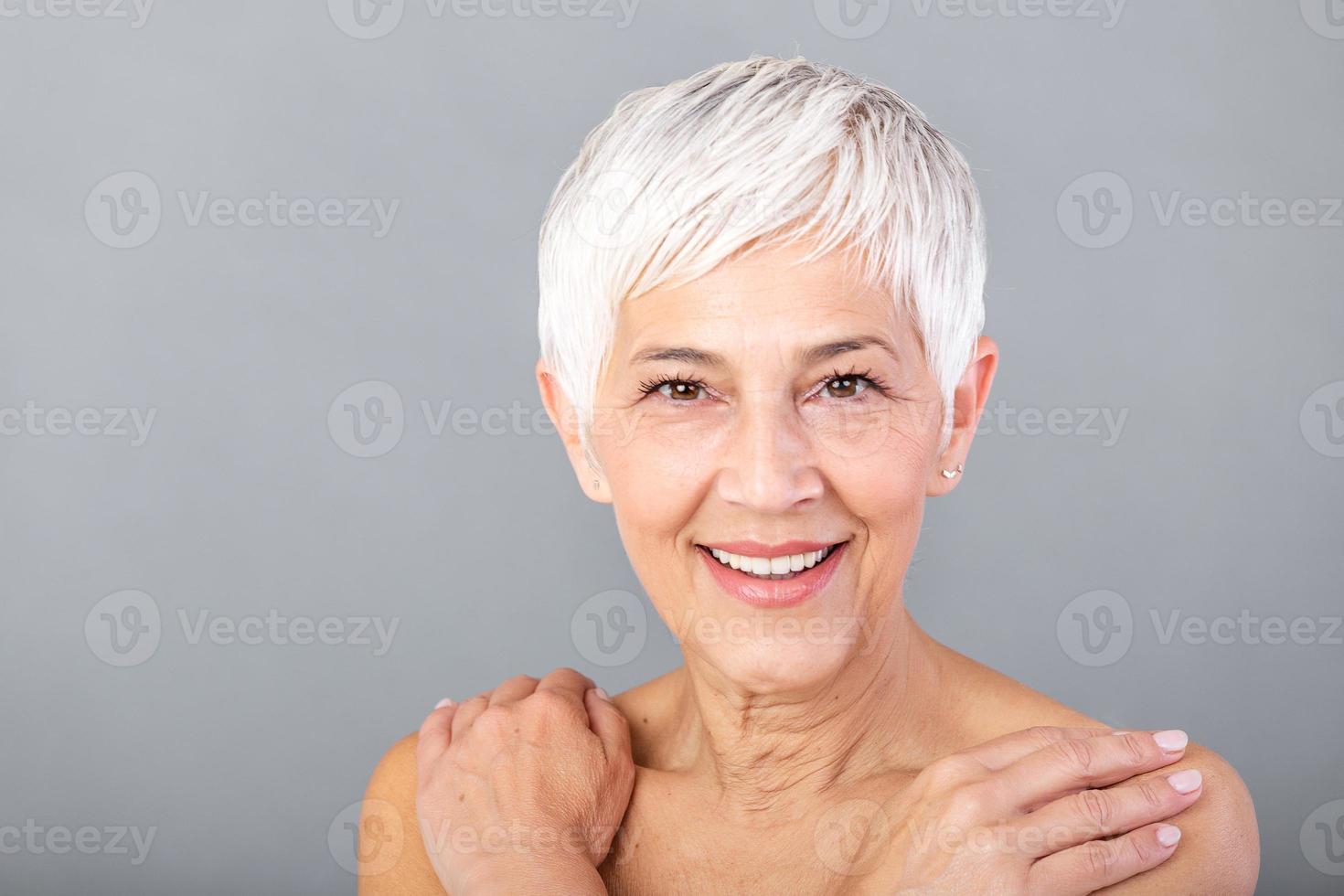 ritratto di un' sorridente anziano donna guardare a telecamera. avvicinamento viso di maturo donna dopo terme trattamento isolato al di sopra di grigio sfondo. anti età concetto. foto