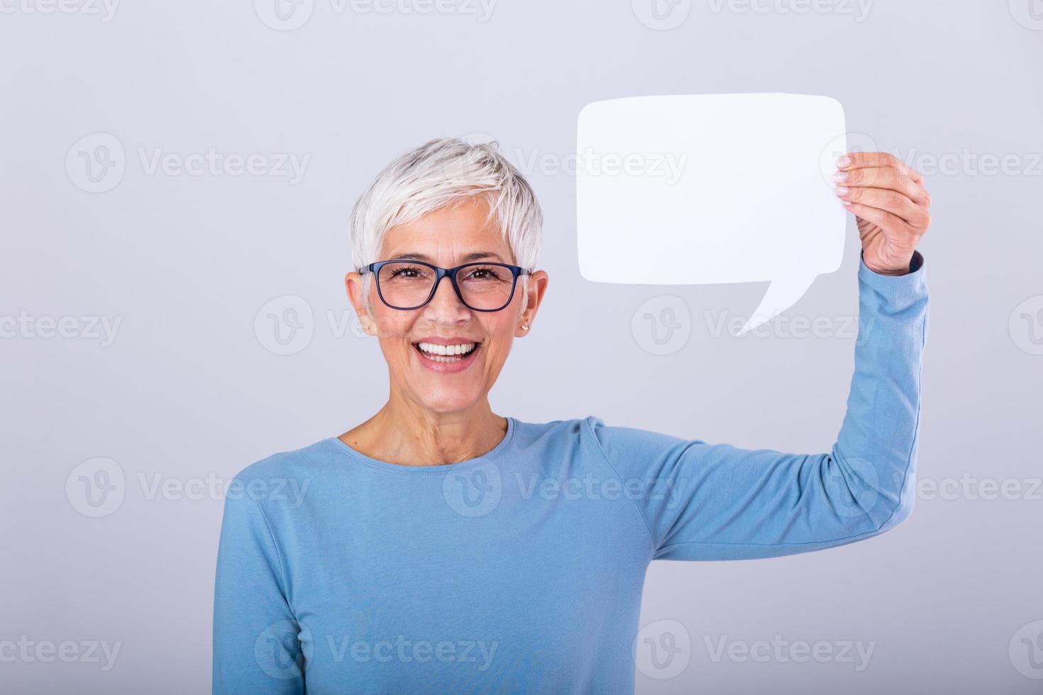 ritratto di un' un eccitato maturo grigio capelli donna mostrando vuoto discorso bolla isolato al di sopra di grigio sfondo. anziano donna Tenere discorso bolla bandiera foto