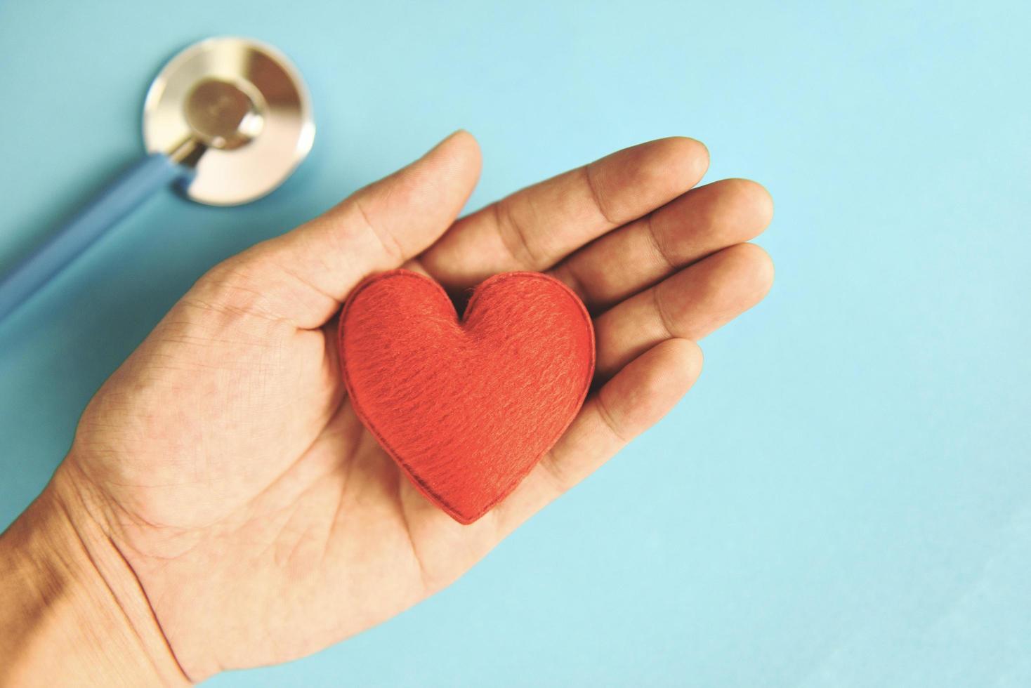 assicurazione Salute concetto - stetoscopio e rosso cuore nel mano assistenza sanitaria su blu sfondo foto