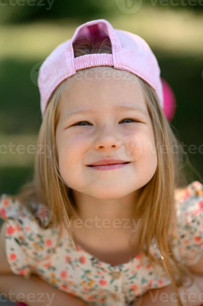 un' poco ragazza 3 anni vecchio nel un' rosa berretto cavalcate un' scooter. estate volta. foto