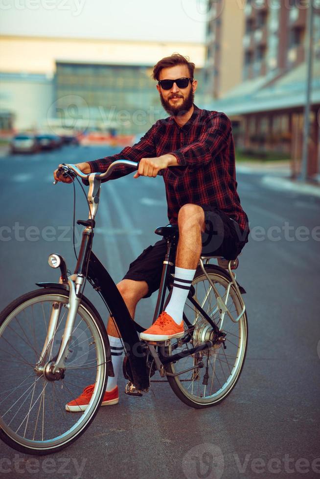 uomo nel occhiali da sole equitazione un' bicicletta su città strada foto