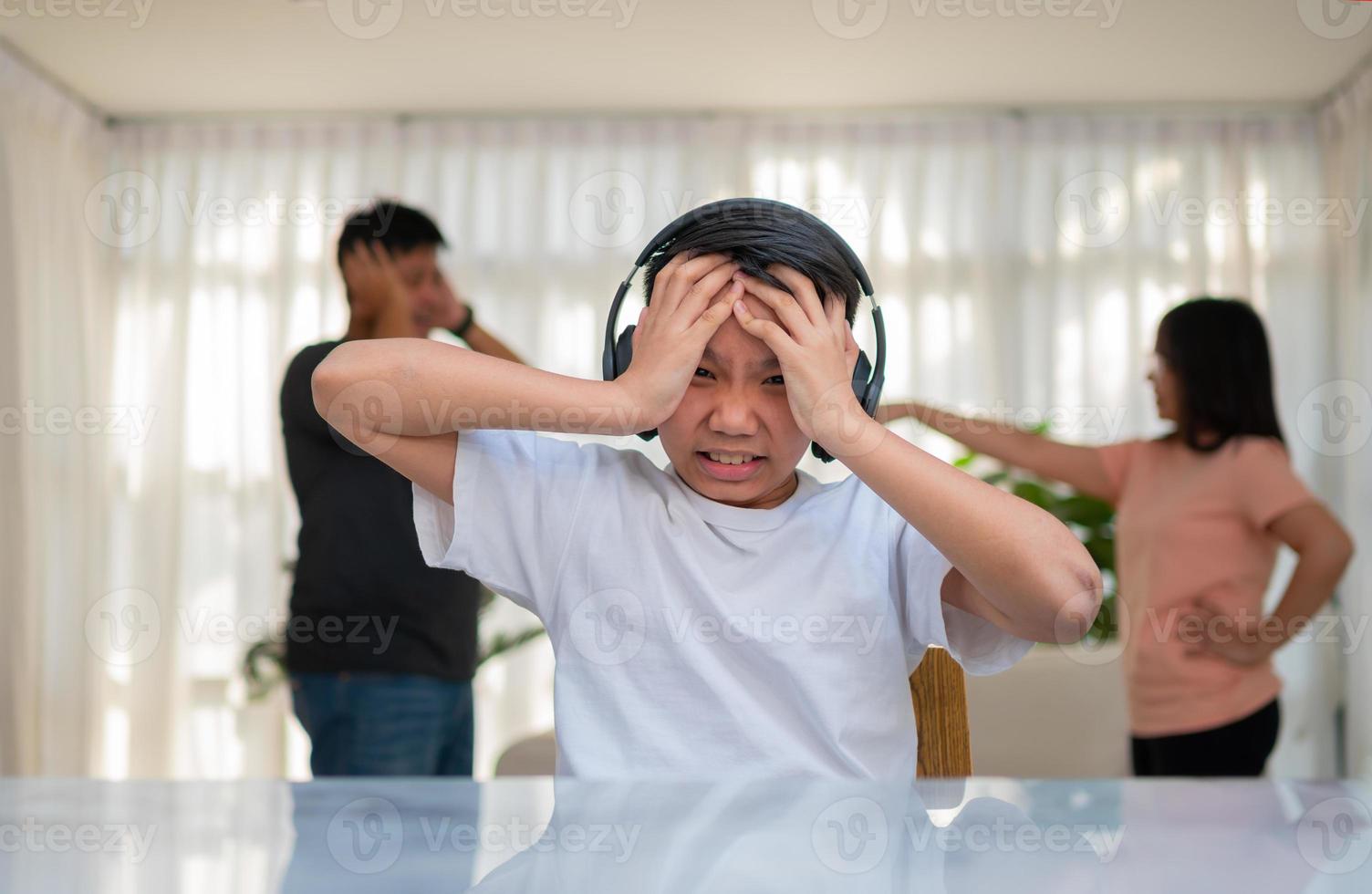 ragazzo asiatico che indossa le cuffie e suona musica ad alto volume. in modo da non sentire litigare mentre i genitori litigano o litigano in casa. problema infelice in famiglia, problemi domestici in famiglia. foto