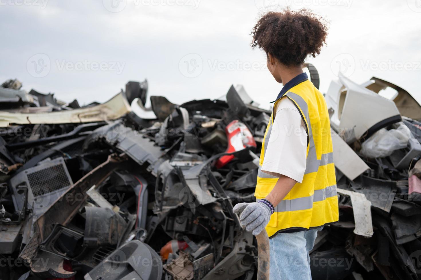 meccanico donna proprietario piccolo attività commerciale ispezionando in piedi nel il auto discarica, sporco maschio riparatore la scelta scorta parti su auto discarica, Usato di veicolo parte per raccolta differenziata nel il rottame cortile box auto. foto