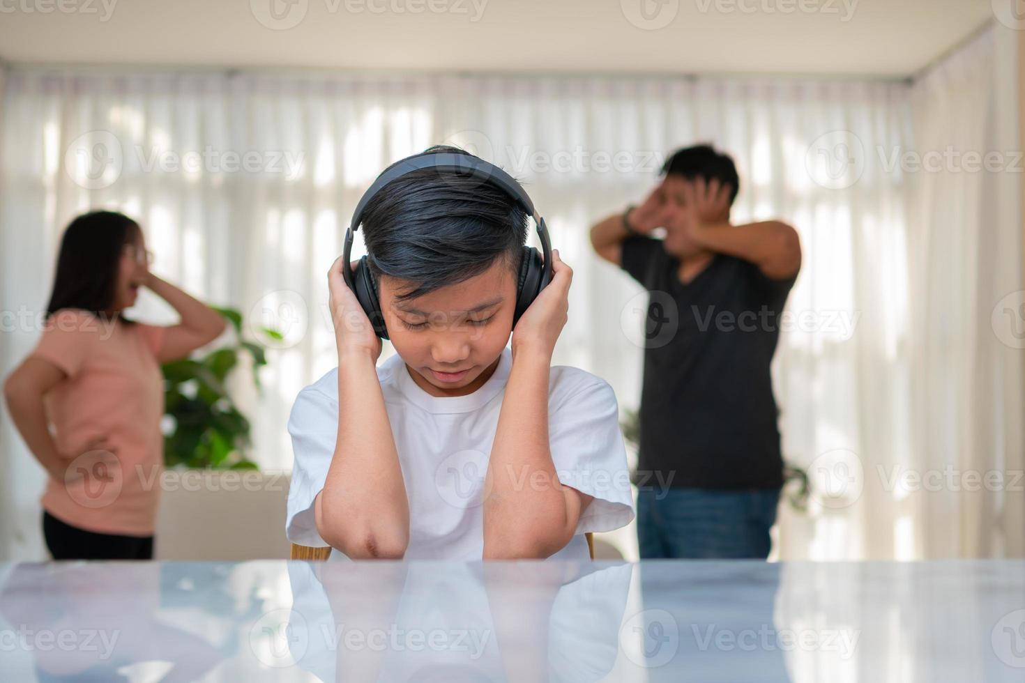 ragazzo asiatico che indossa le cuffie e suona musica ad alto volume. in modo da non sentire litigare mentre i genitori litigano o litigano in casa. problema infelice in famiglia, problemi domestici in famiglia. foto