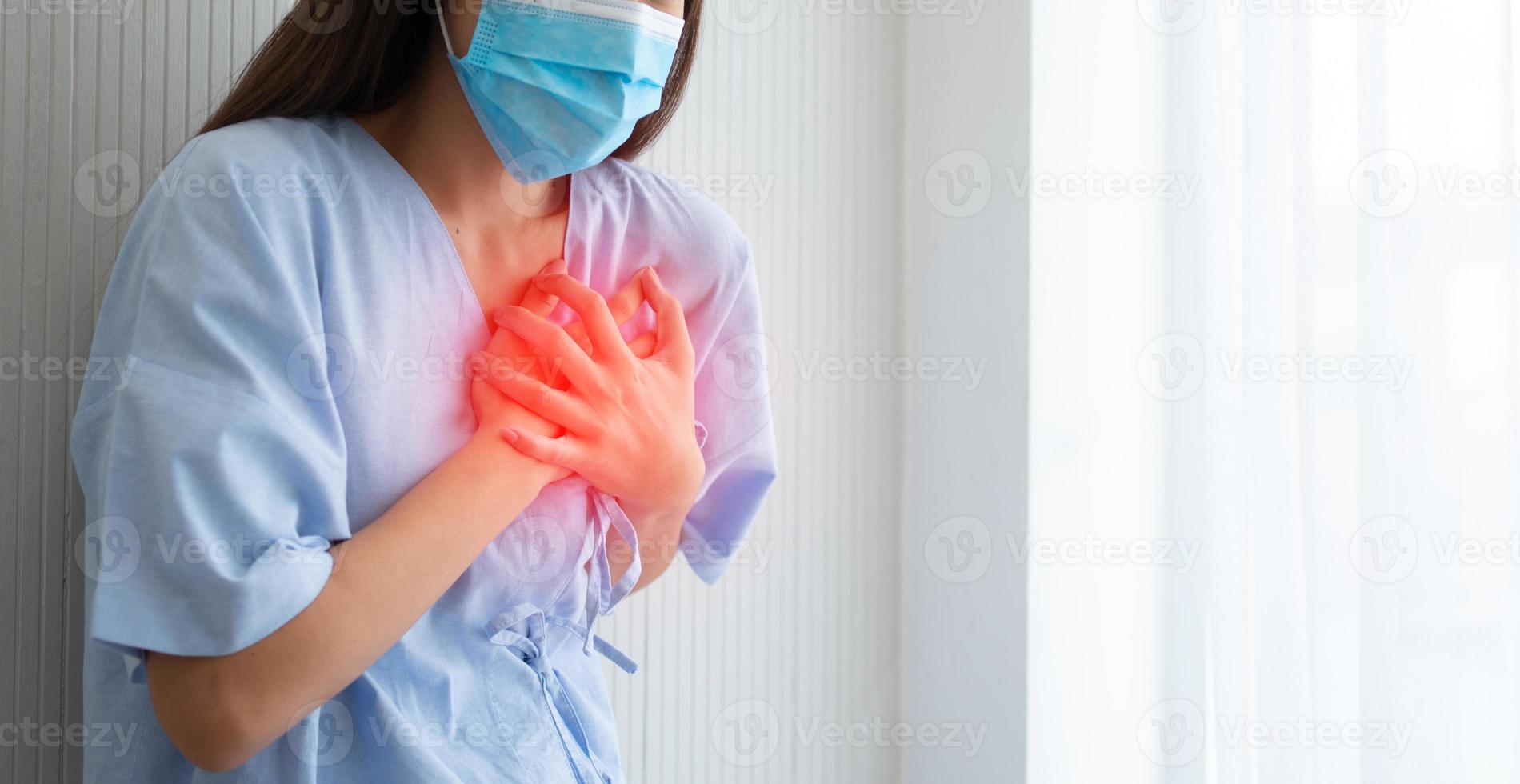 femmina paziente indossare un' maschera e mano Tenere il petto dovuto per cuore attacco sintomi foto