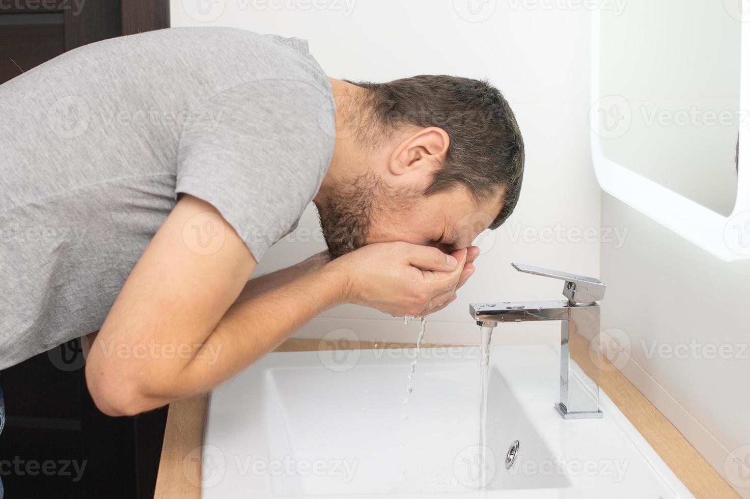 il uomo Appoggiato al di sopra di per il lavabo per lavare il suo viso foto