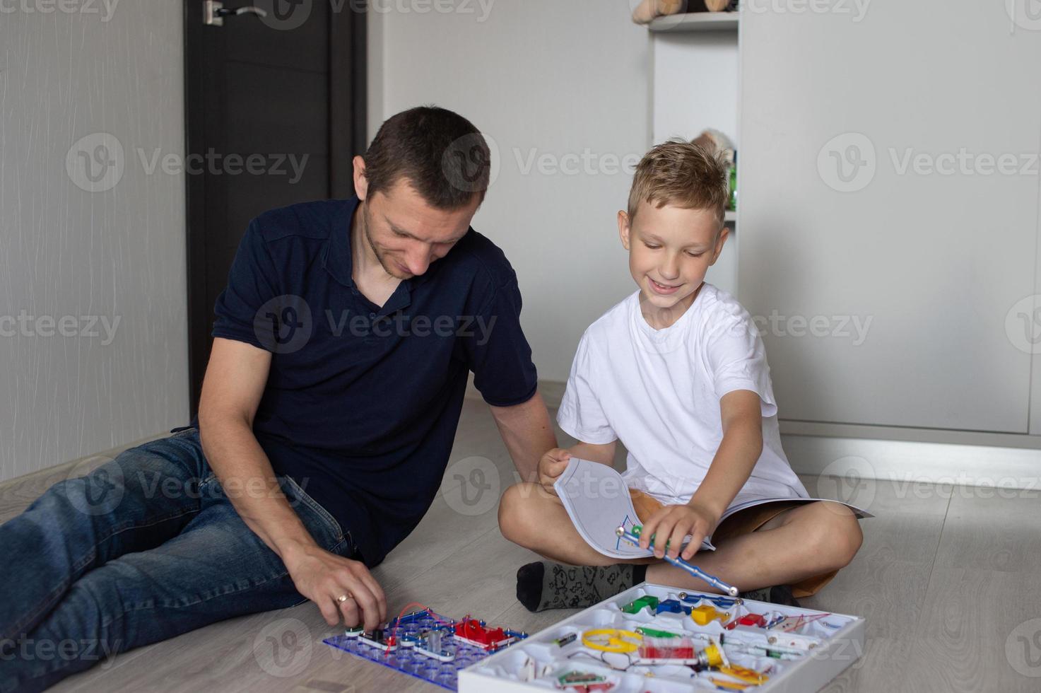 un' carino ragazzo nel un' bianca maglietta raccoglie un elettrico progettista con il suo papà nel il camera foto