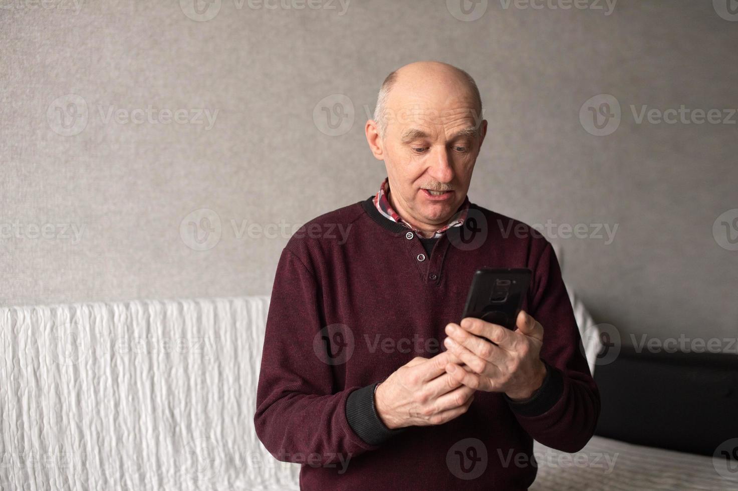 un adulto uomo con un' baffi e un' Calvo testa cerca per girare su il Telefono. uso gadget foto