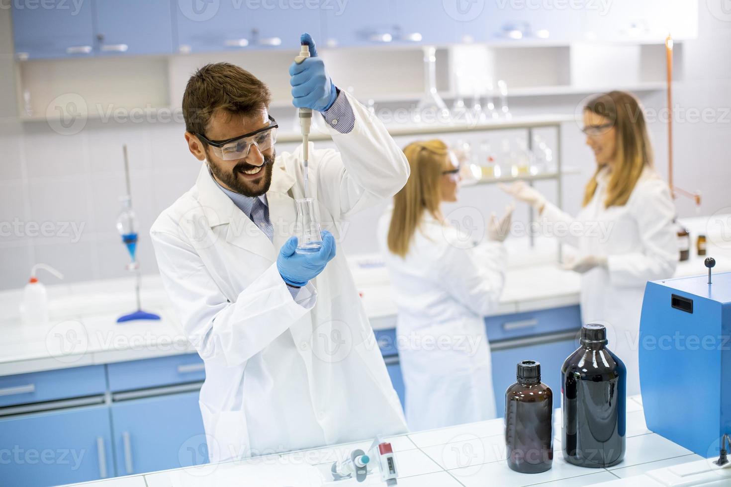 giovani ricercatori in indumenti da lavoro protettivi in piedi in laboratorio e analizzando il pallone con liquido foto