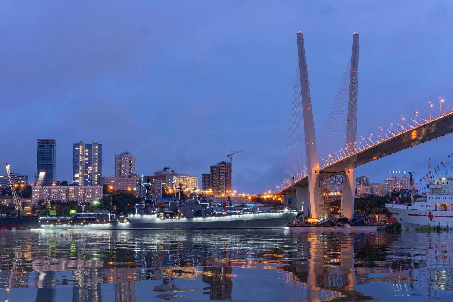 paesaggio urbano notturno di navi in acqua alla baia del corno d'oro e il ponte d'oro a vladivostok, russia foto