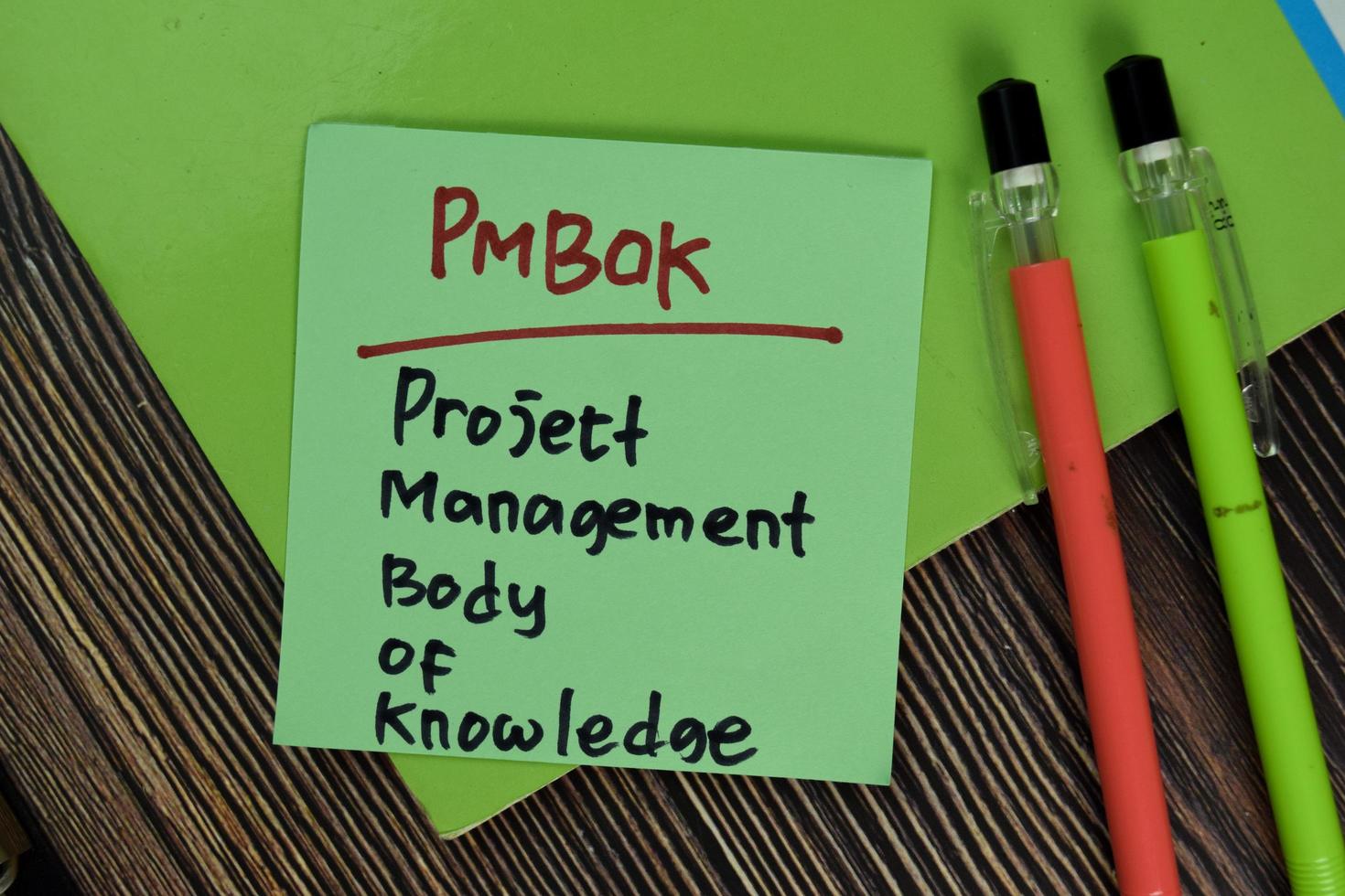 pmbok - corpo di conoscenza della gestione del progetto scritto su una nota adesiva isolata su un tavolo di legno foto