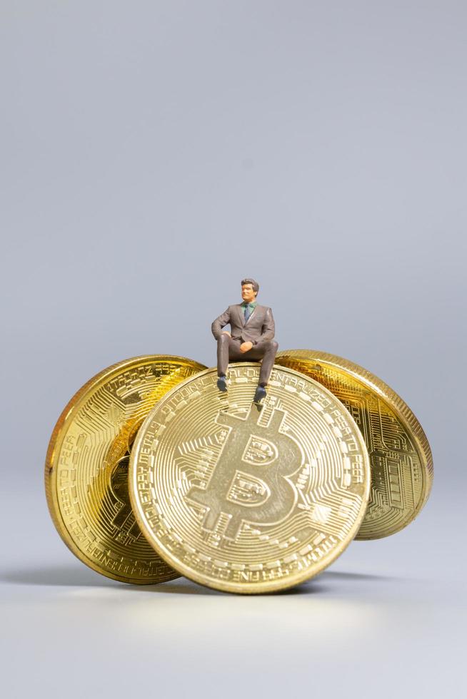 imprenditore in miniatura seduto su monete bitcoin, futuro concetto di investimento foto