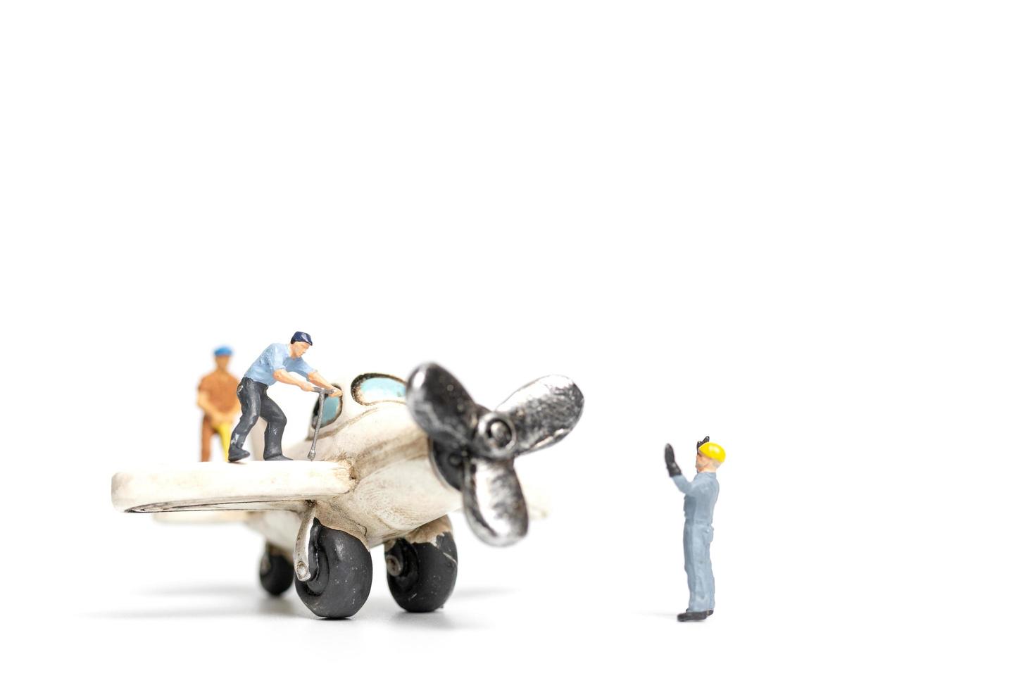 lavoratori in miniatura che riparano un aeroplano giocattolo su uno sfondo bianco foto