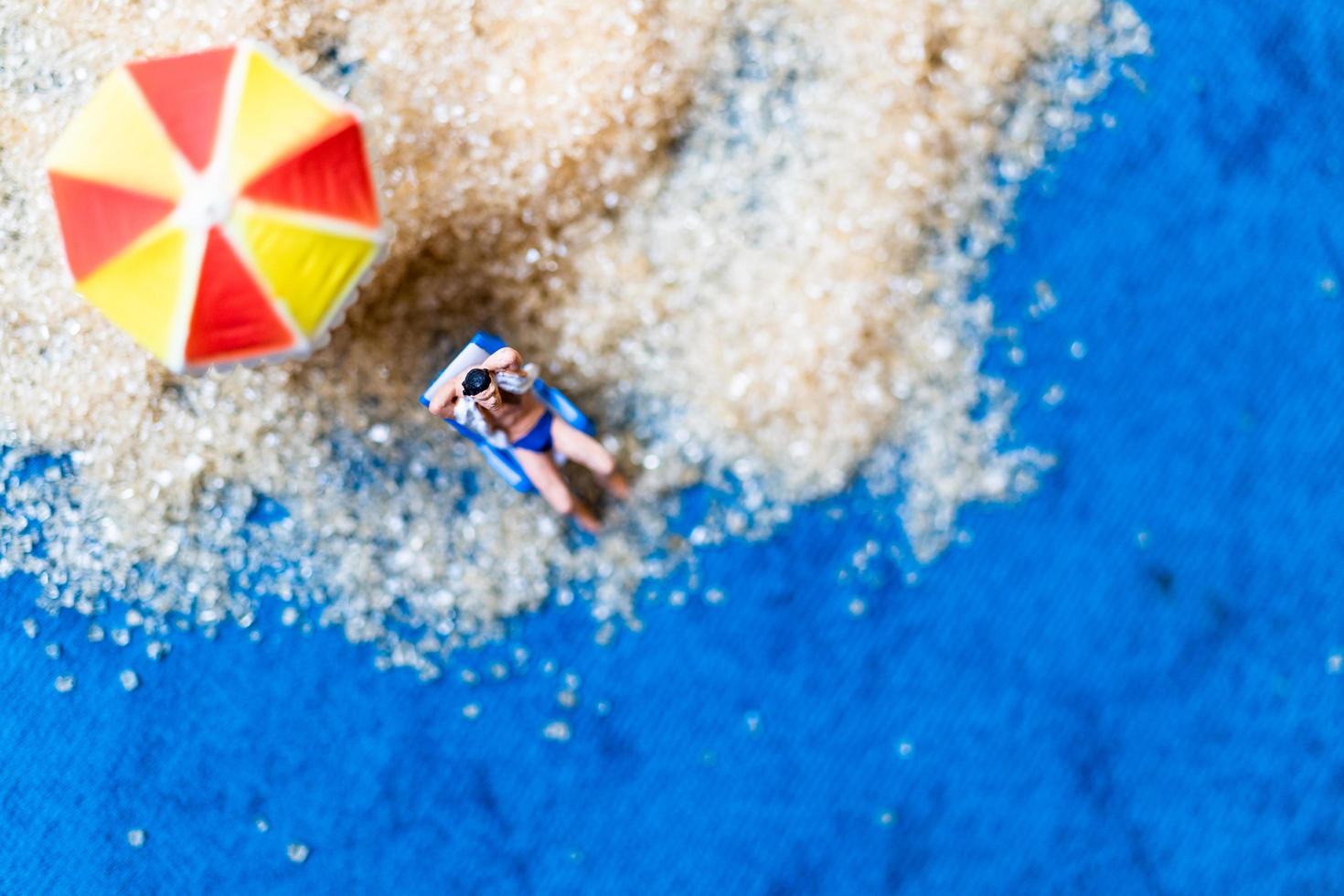 persone in miniatura che prendono il sole su una spiaggia, concetto di estate foto