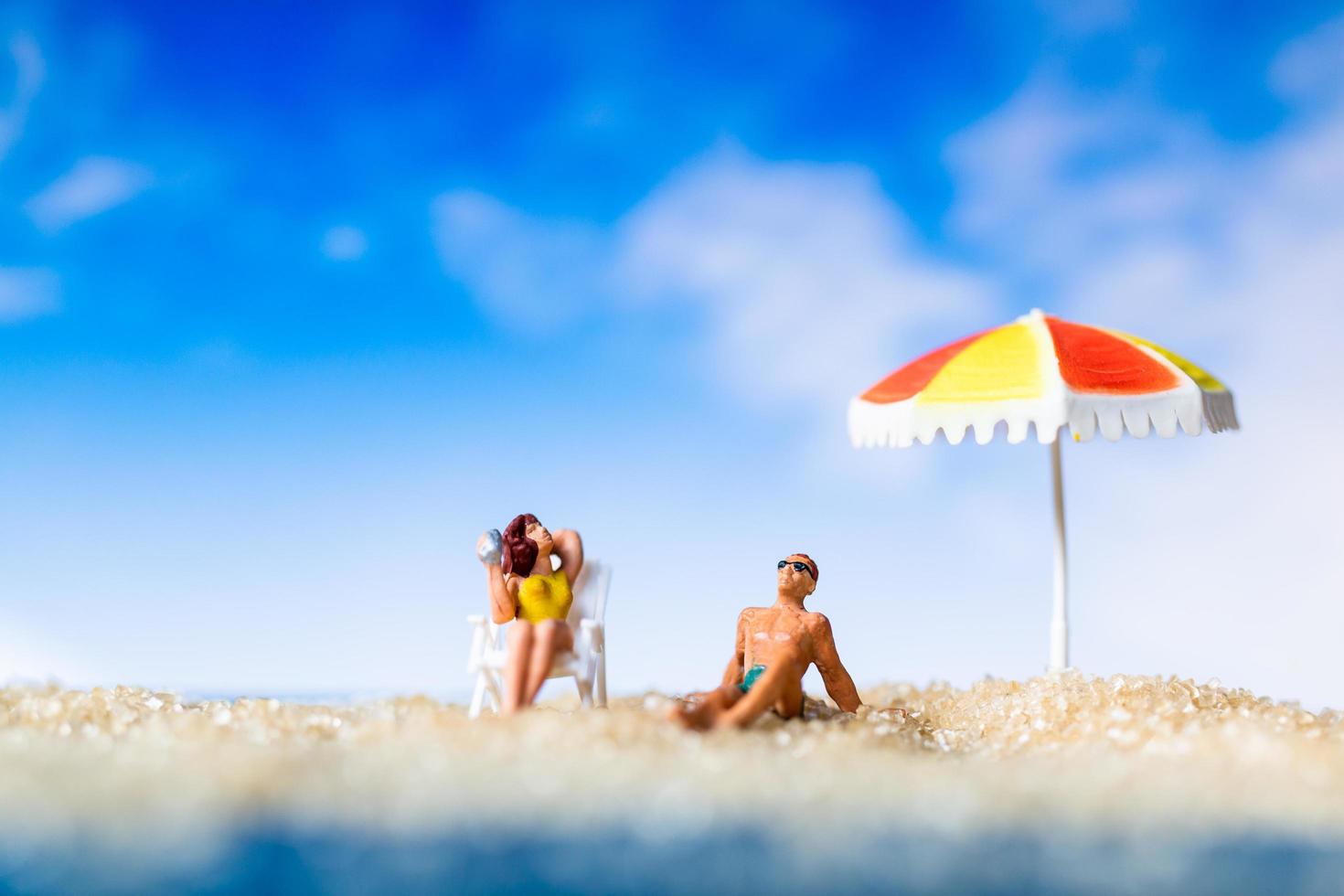 persone in miniatura che prendono il sole su una spiaggia, concetto di estate foto