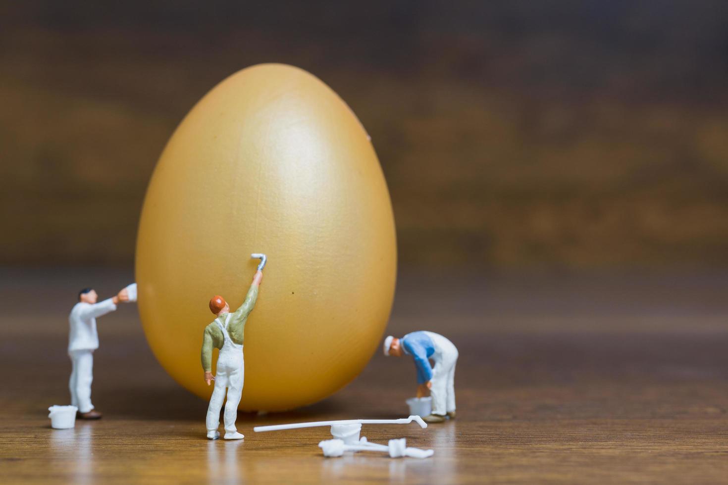 pittori in miniatura che dipingono le uova di Pasqua per la Pasqua su uno sfondo di legno foto