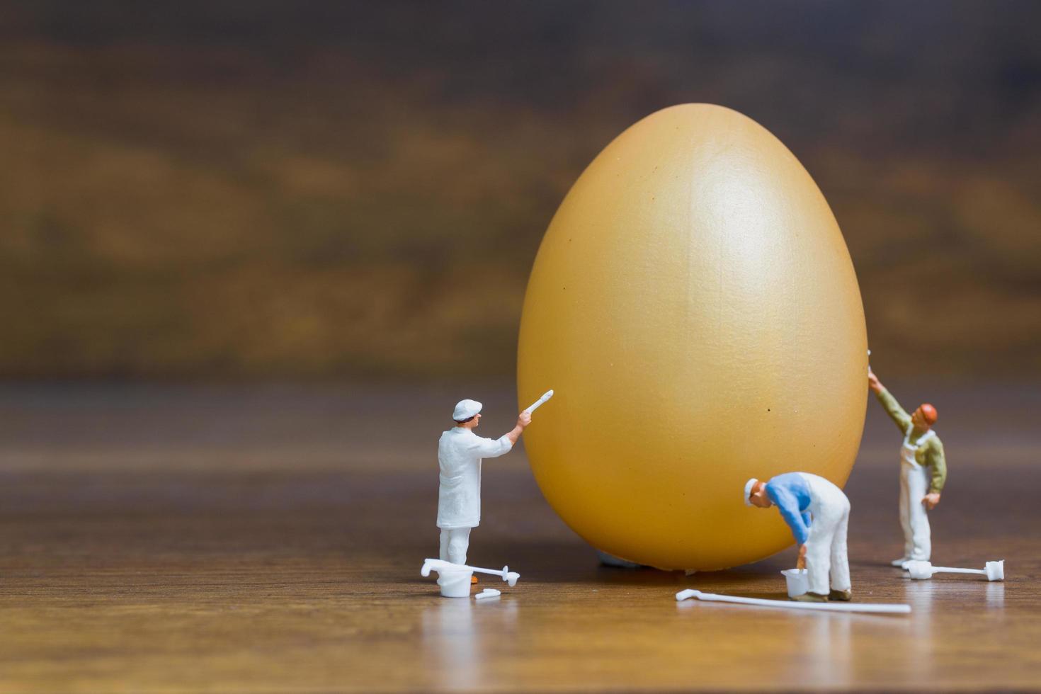 pittori in miniatura che dipingono le uova di Pasqua per la Pasqua su uno sfondo di legno foto