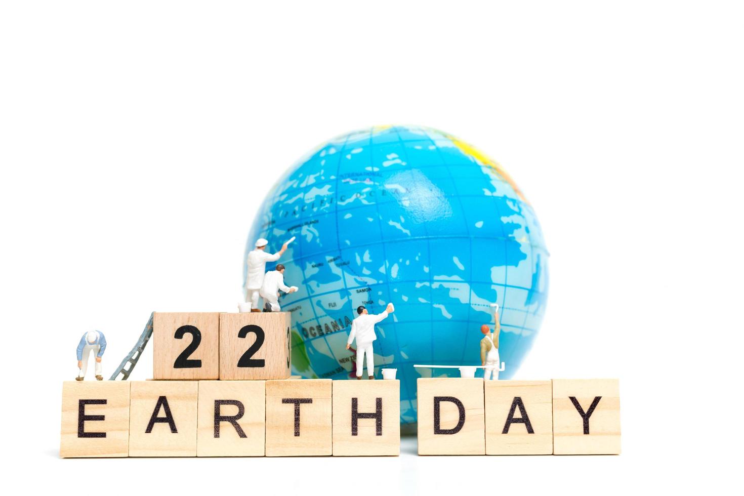 pittori in miniatura che dipingono su un globo con blocchi di legno che mostrano la Giornata della Terra 22 su uno sfondo bianco, concetto della Giornata della Terra foto