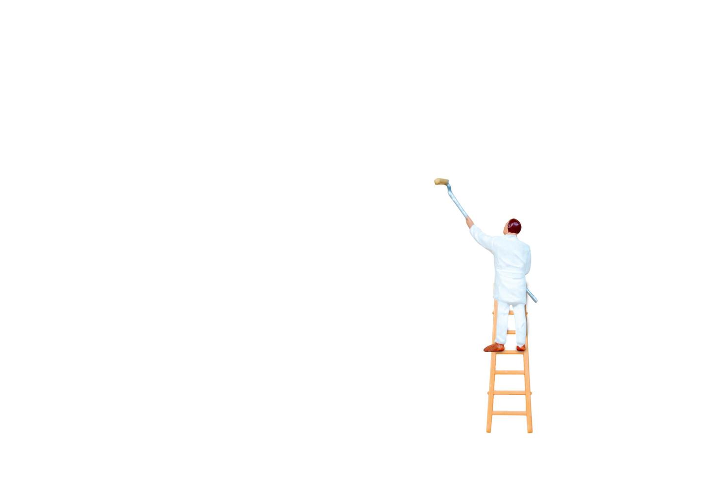 persona in miniatura con una scala che tiene un pennello davanti a uno sfondo di muro bianco foto