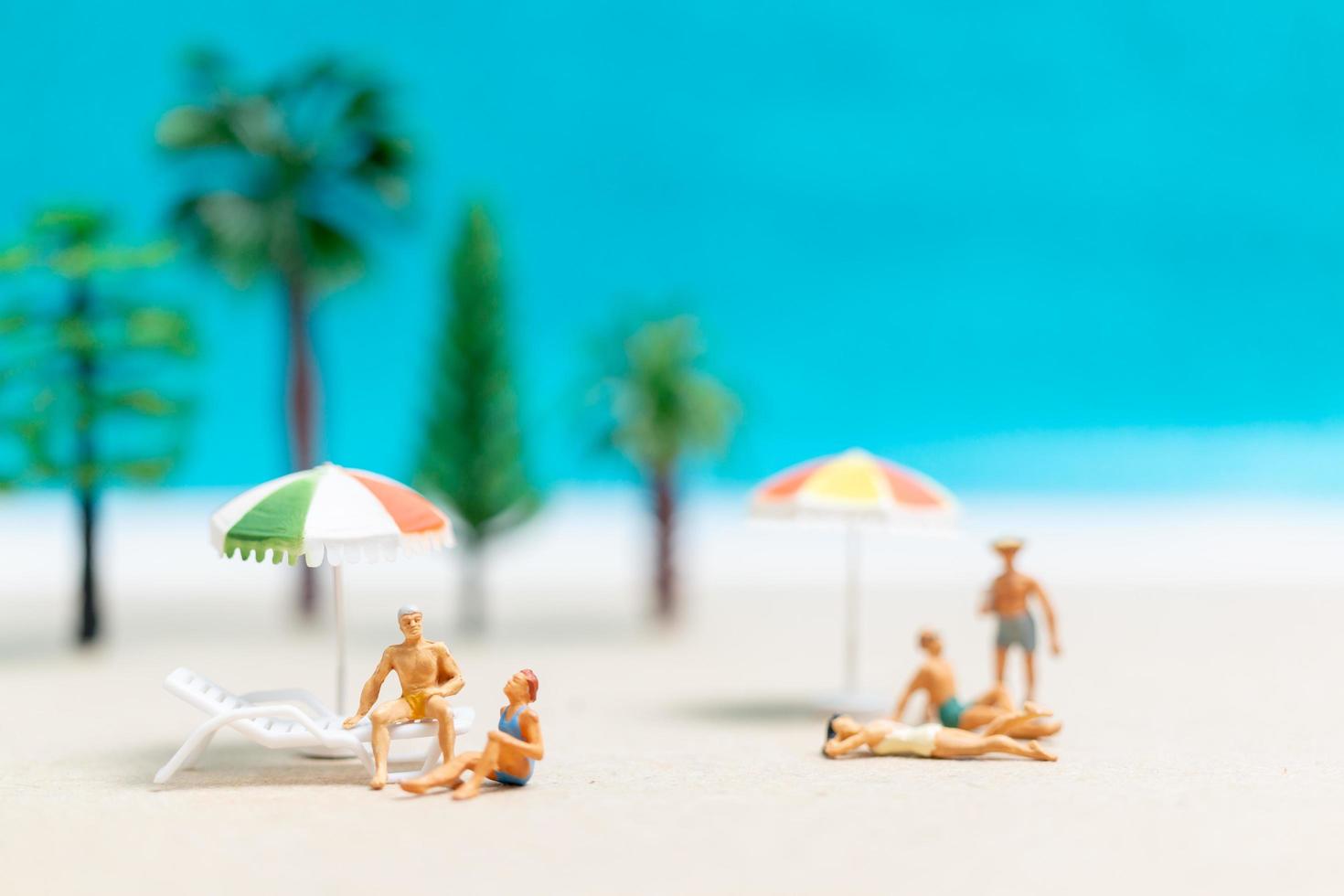 persone in miniatura che indossano costumi da bagno che si rilassano su una spiaggia con uno sfondo blu foto