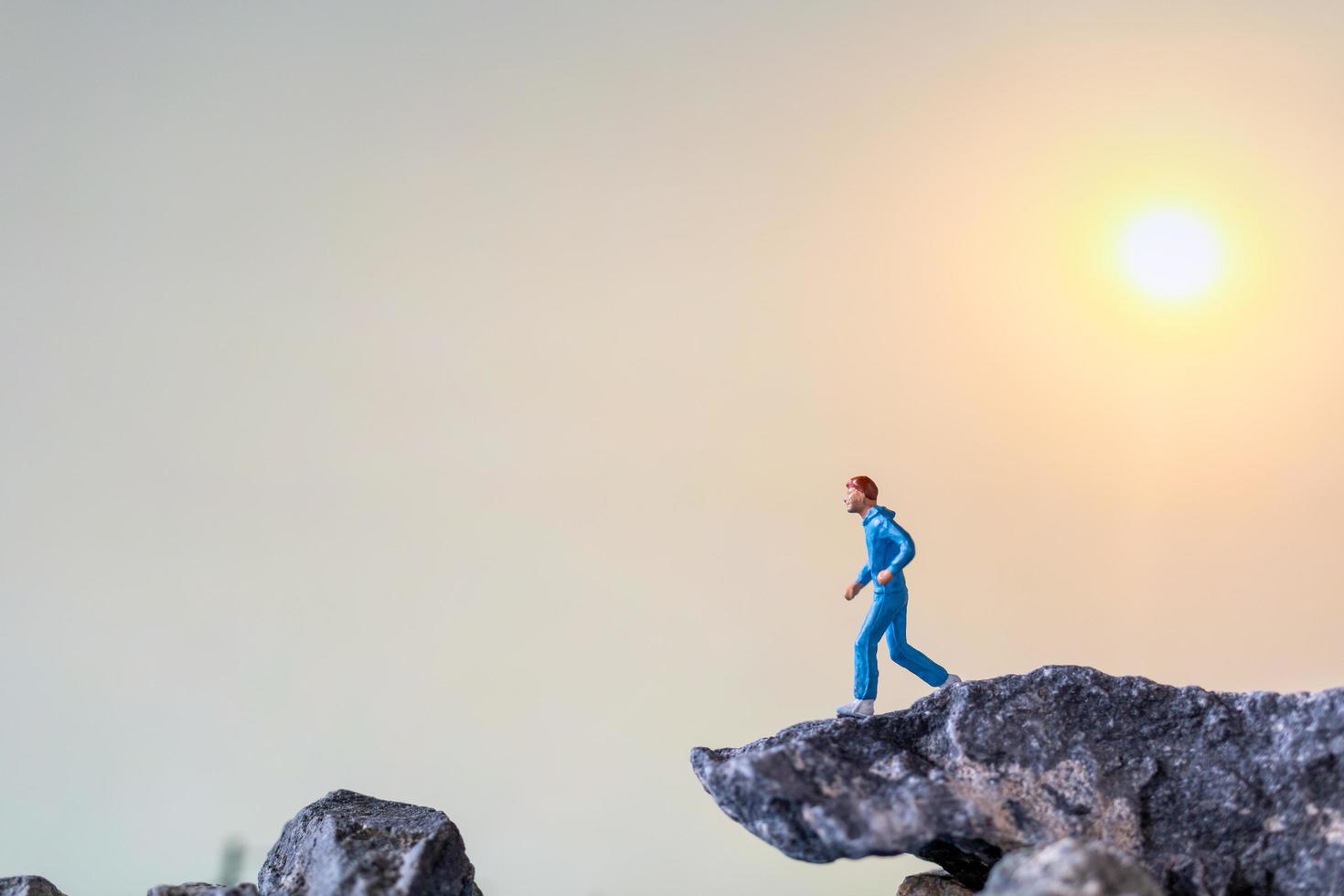 persone in miniatura in esecuzione su una scogliera rocciosa con sfondo della natura, concetto di salute e stile di vita foto