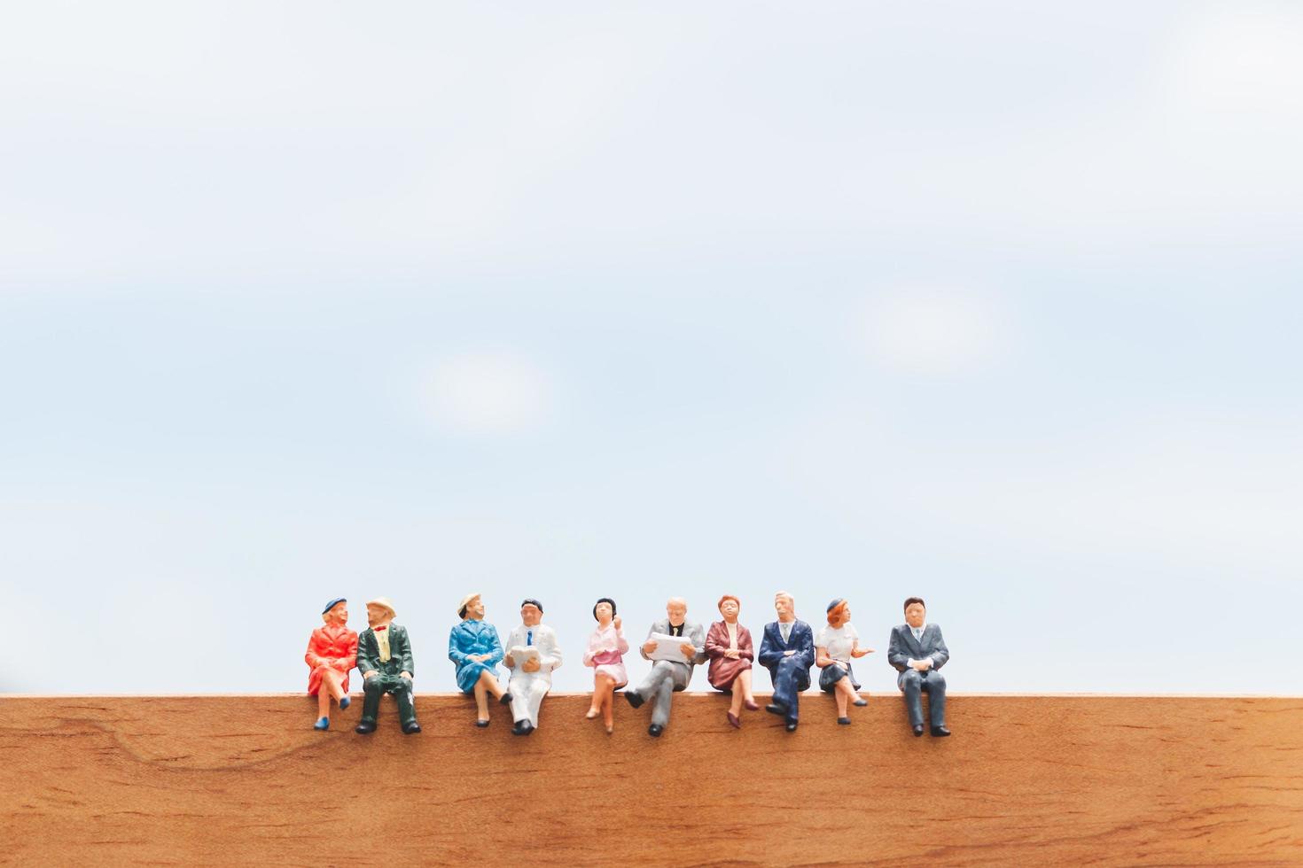 gruppo in miniatura di uomini d'affari seduti su un pavimento di legno con uno sfondo blu del cielo foto