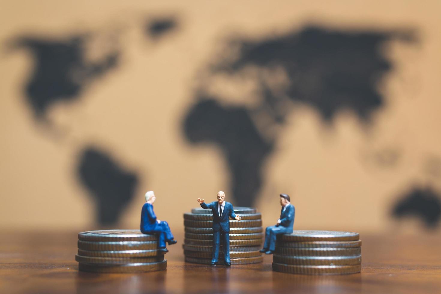 uomini d'affari in miniatura su una pila di monete con una mappa del mondo in background, denaro e concetto di successo aziendale finanziario foto