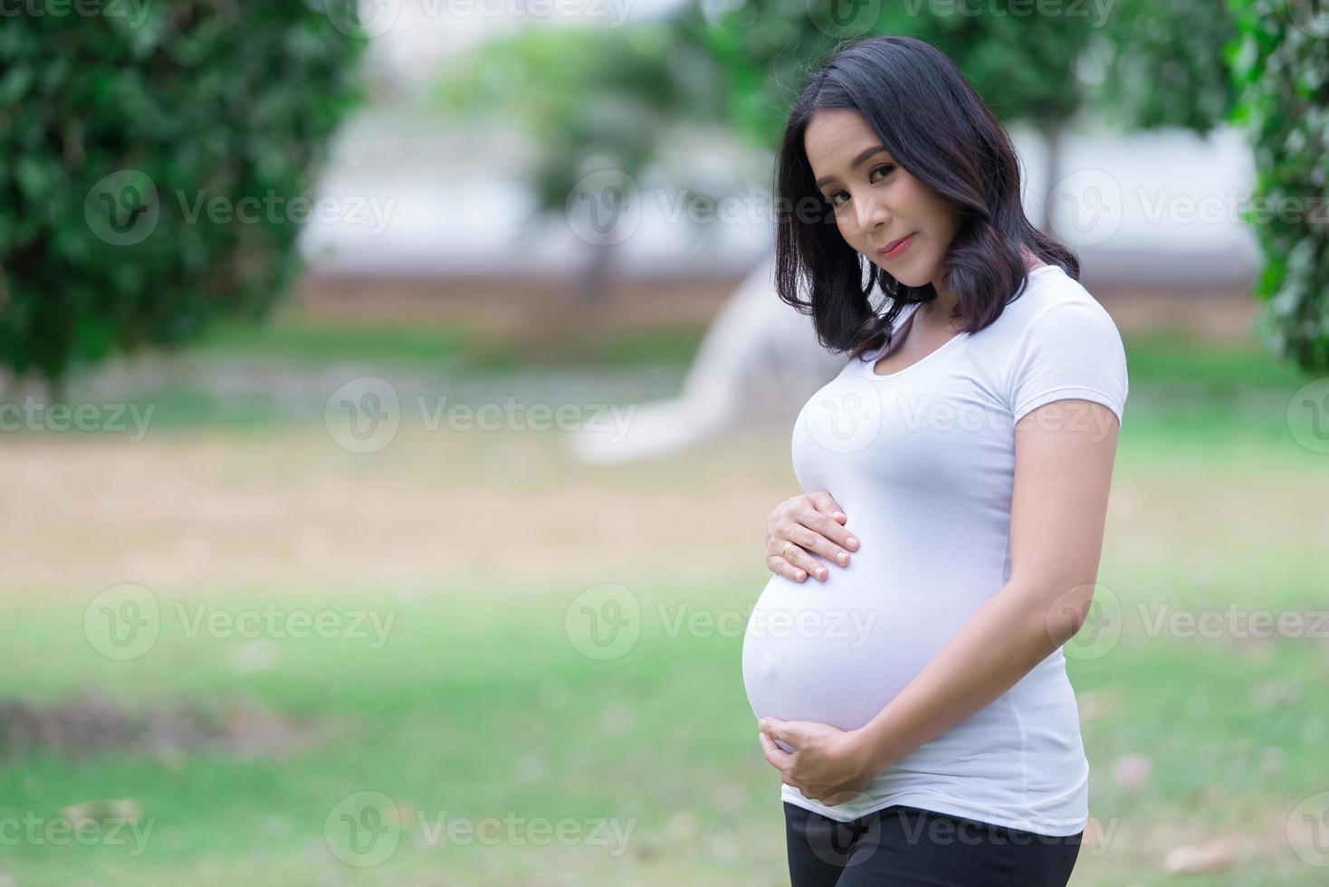 ritratto di asiatico bellissimo incinta donna a il parco, Tailandia gente, felice donna concetto, lei uso mano toccare sua pancia, madre giorno concetto foto