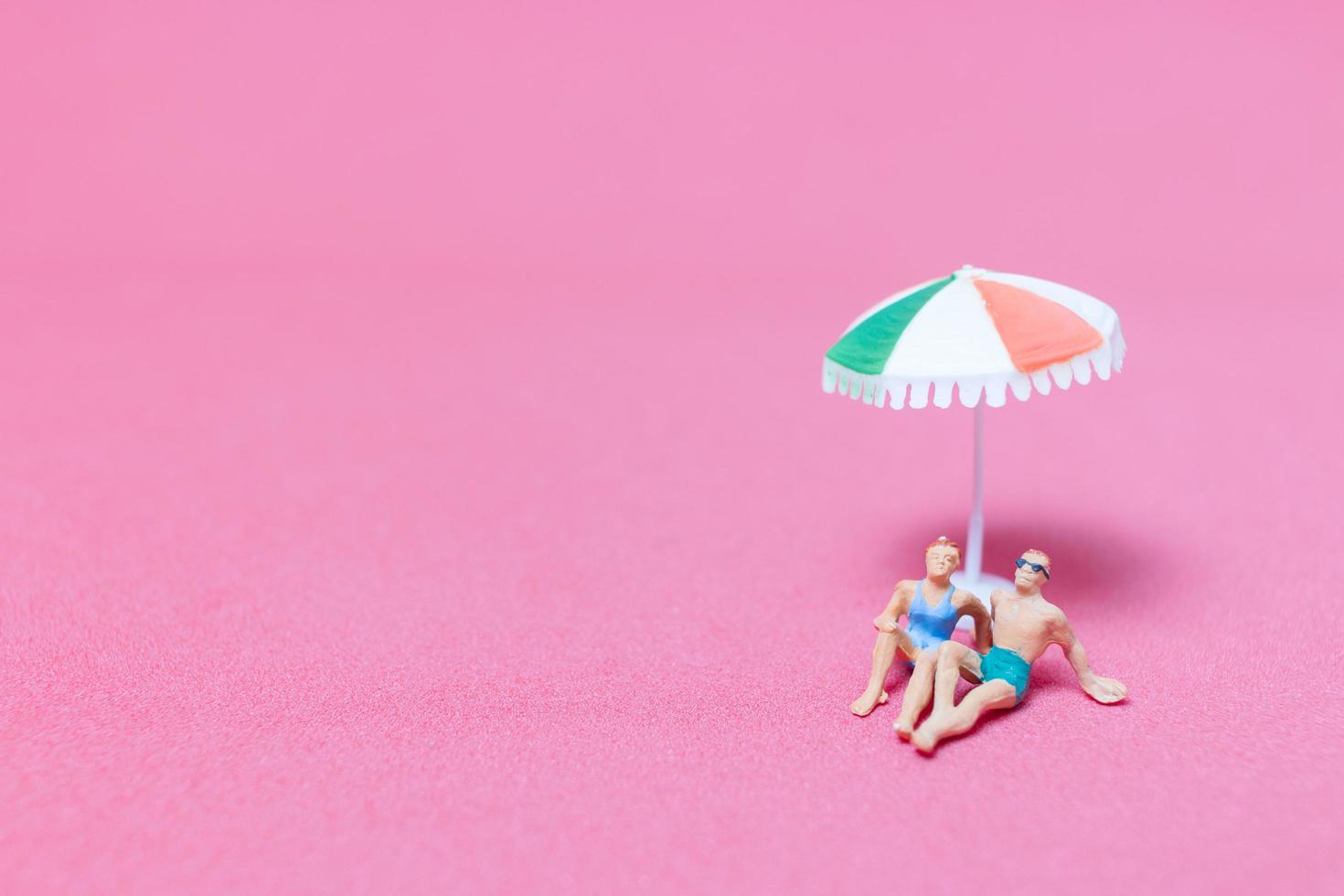 persone in miniatura che indossano costumi da bagno che si rilassano su uno sfondo rosa foto
