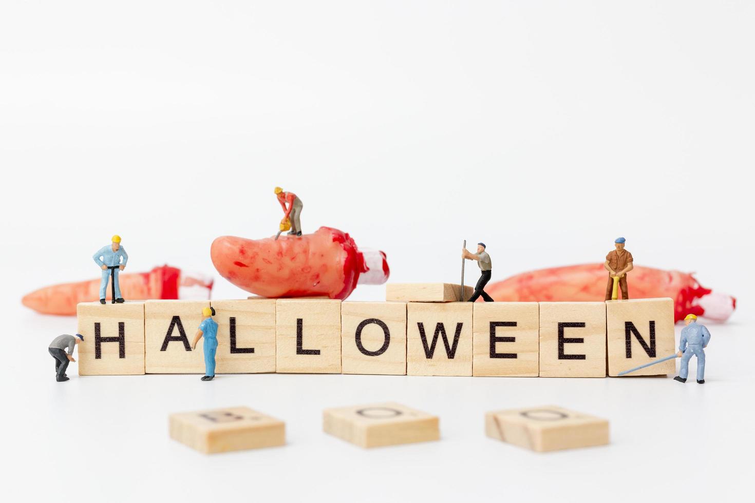 lavoratori in miniatura che collaborano per creare oggetti di scena per la festa di Halloween con blocchi di legno con il testo Halloween su uno sfondo bianco foto