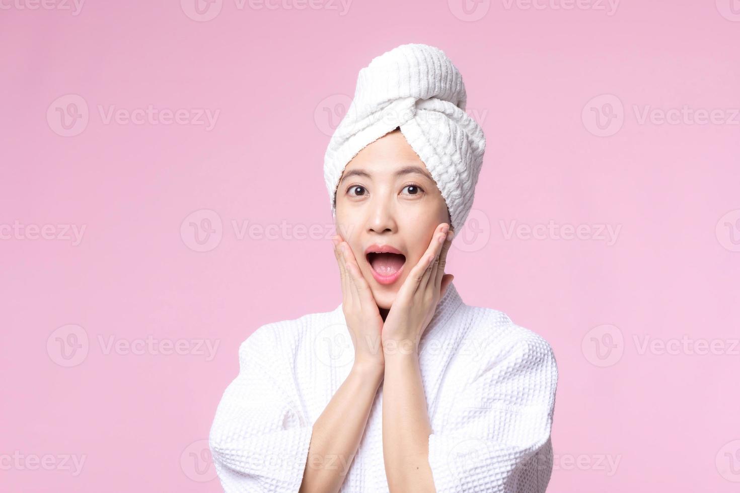 bellissimo giovane asiatico donna contento Sorridi viso con mano o dito gesto segni nel accappatoio e doccia asciugamano mostrando vuoto spazio isolato su rosa sfondo. foto