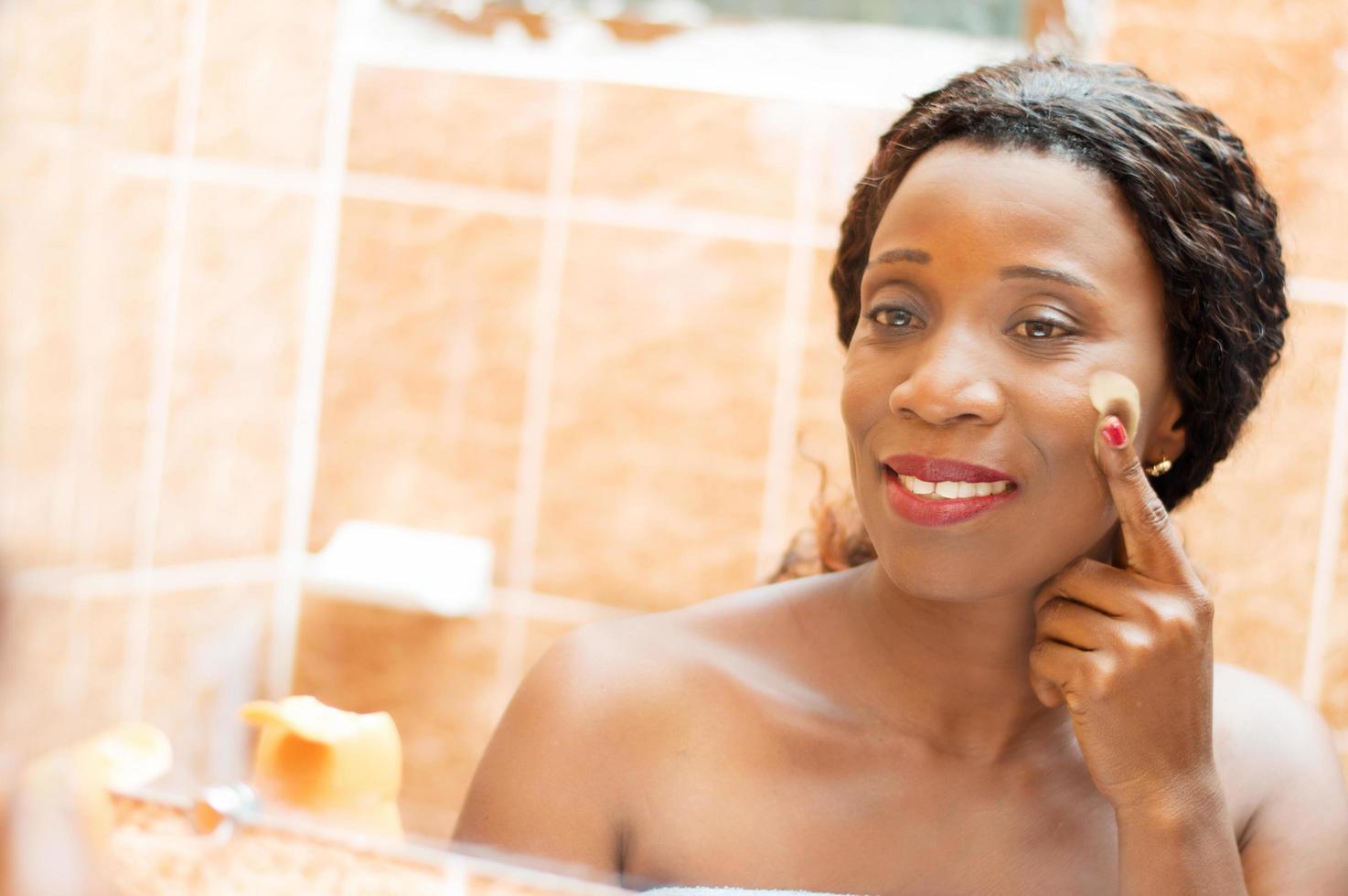 felice giovane donna applica la crema sul viso in bagno foto