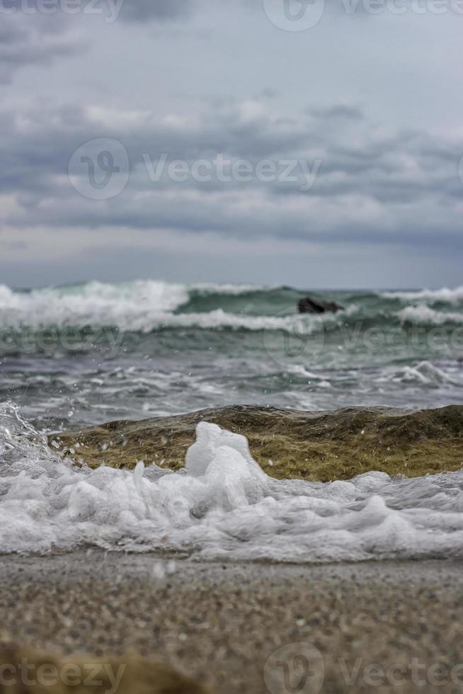 spruzzo di mare schiuma su il riva di il nero mare. vicino su mare acqua onde con bolle su il sabbia spiaggia foto