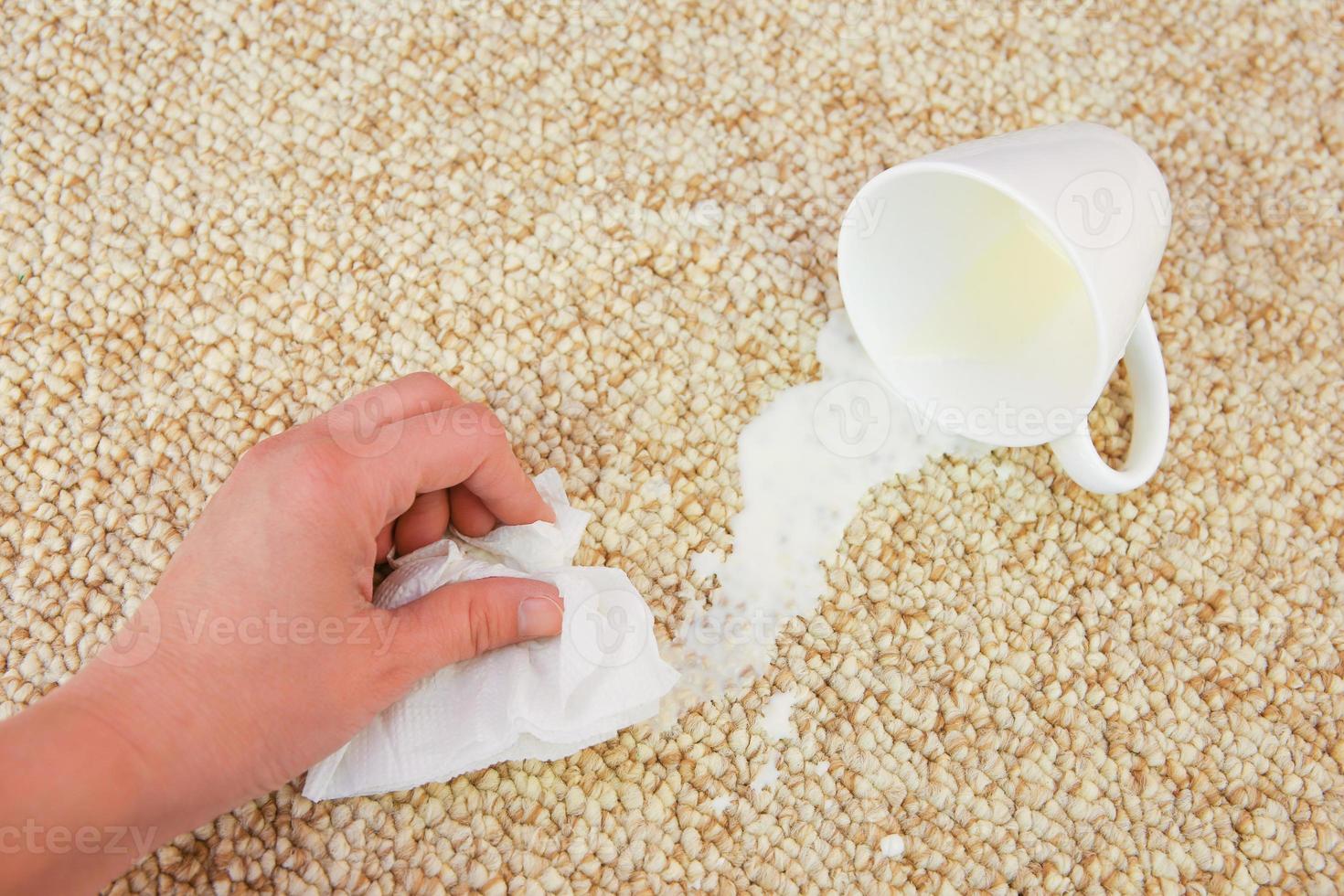 bicchiere di latte abbattere e rovesciato su pavimento. femmina mano pulisce tappeto con tovagliolo. foto