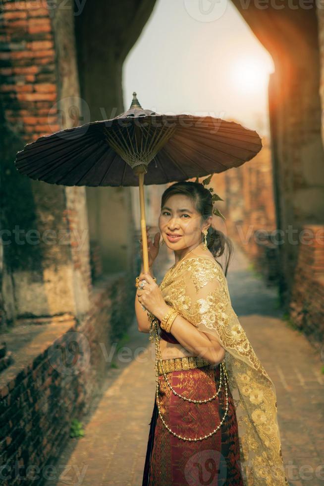 bellissimo asiatico donna indossare tailandese tradizione Abiti Tenere bambù ombrello in piedi nel vecchio tempio a ayutthaya mondo eredità luogo di unesco centrale di Tailandia foto