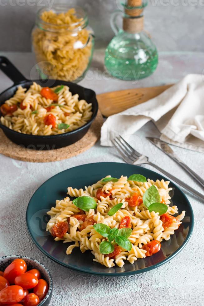 pronto per mangiare pasta con pomodori e basilico su un' piatto e ingredienti su il tavolo. mediterraneo cucina. avvicinamento. verticale Visualizza foto