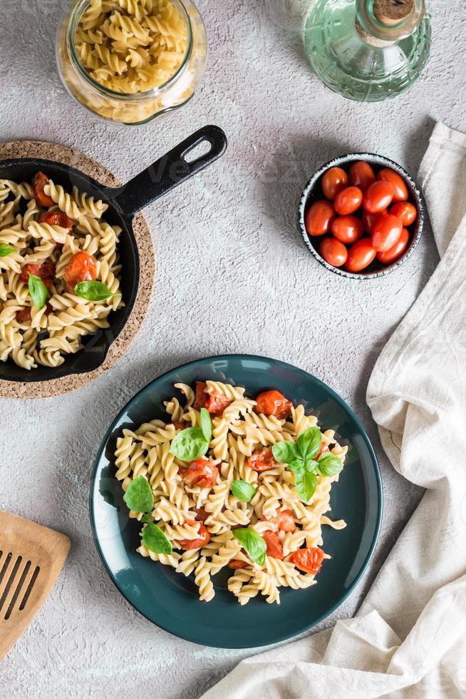 un' piatto di pasta con pomodori e basilico su un' piatto e cucinando ingredienti su il tavolo. mediterraneo cucina. verticale e superiore Visualizza foto