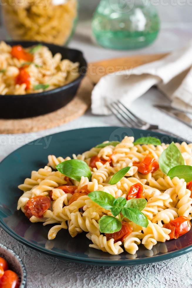 un' piatto di pasta con pomodori e basilico su un' piatto e cucinando ingredienti su il tavolo. mediterraneo cucina. verticale Visualizza. avvicinamento foto