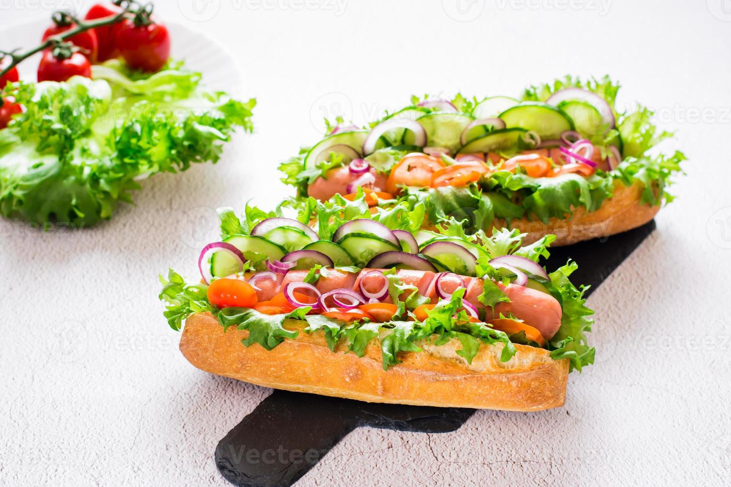 pronto per mangiare caldo cani con salsiccia, cetriolo, pomodoro e erbe aromatiche su un' ardesia su il tavolo. veloce cibo per un' merenda. foto