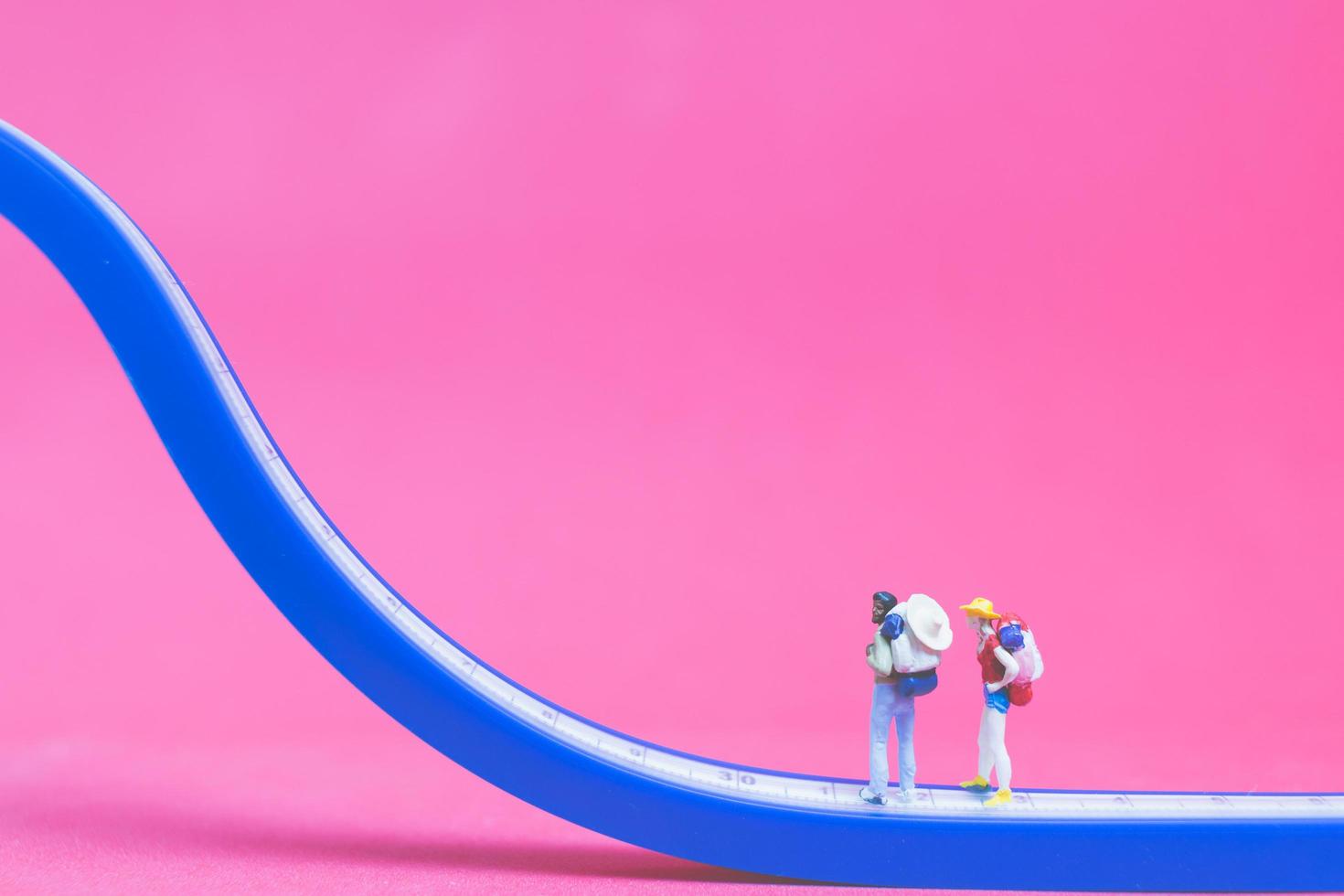 coppia in miniatura di viaggiatori su un ponte con uno sfondo rosa foto