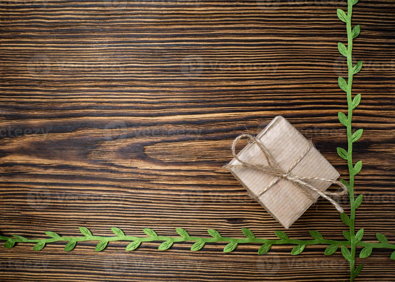 regalo. un' scatola di kraft carta legato con iuta corda su un' vecchio, di legno sfondo decorato con verde nastro con le foglie foto