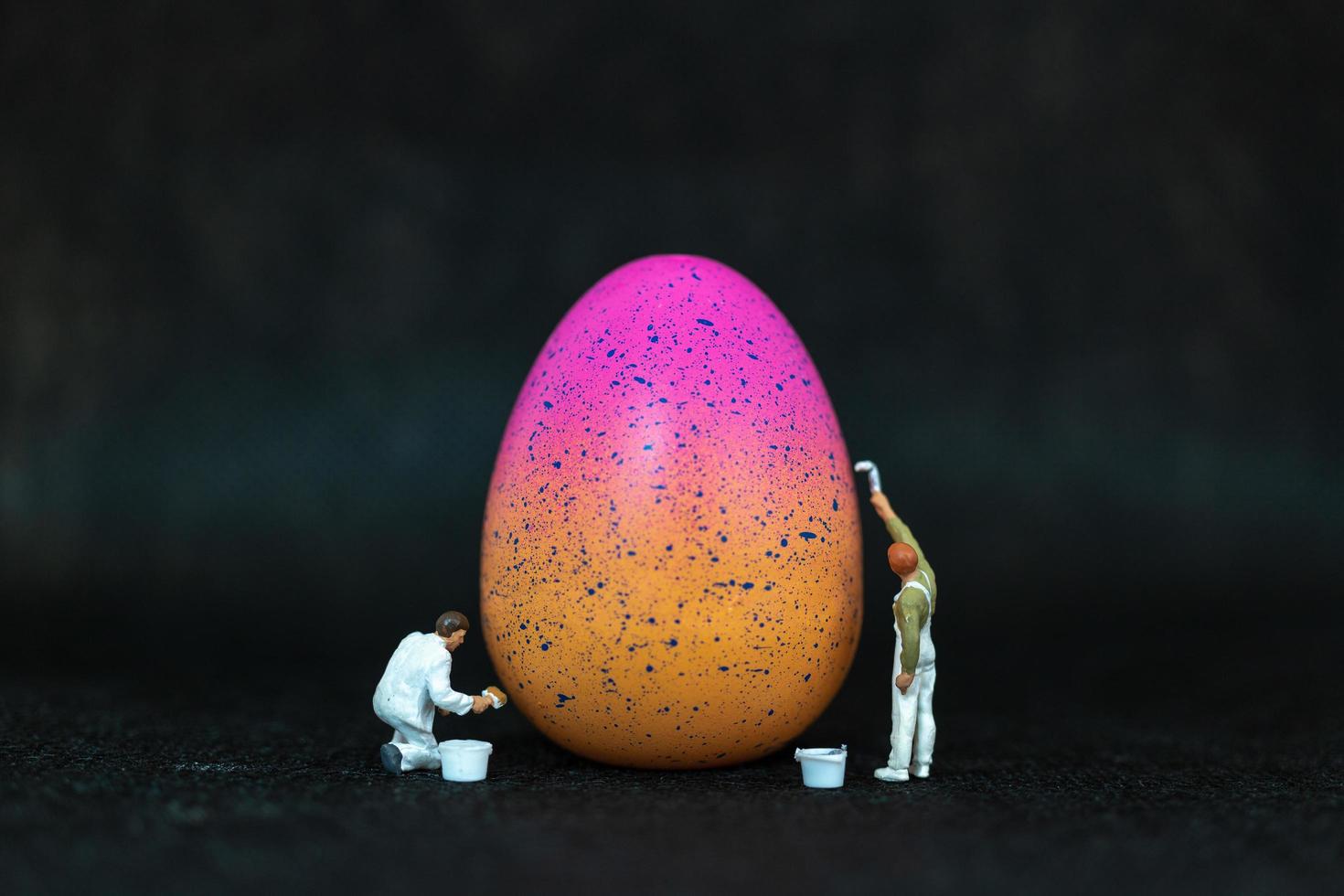 persone in miniatura che dipingono le uova di Pasqua per il giorno di Pasqua su uno sfondo nero foto