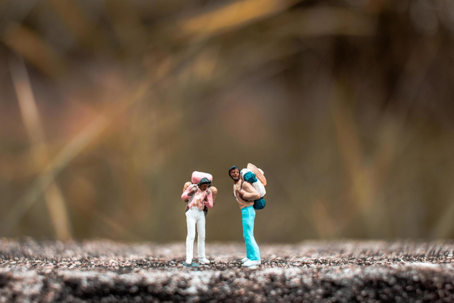 backpackers in miniatura in piedi su un pavimento di cemento con uno sfondo di natura bokeh foto