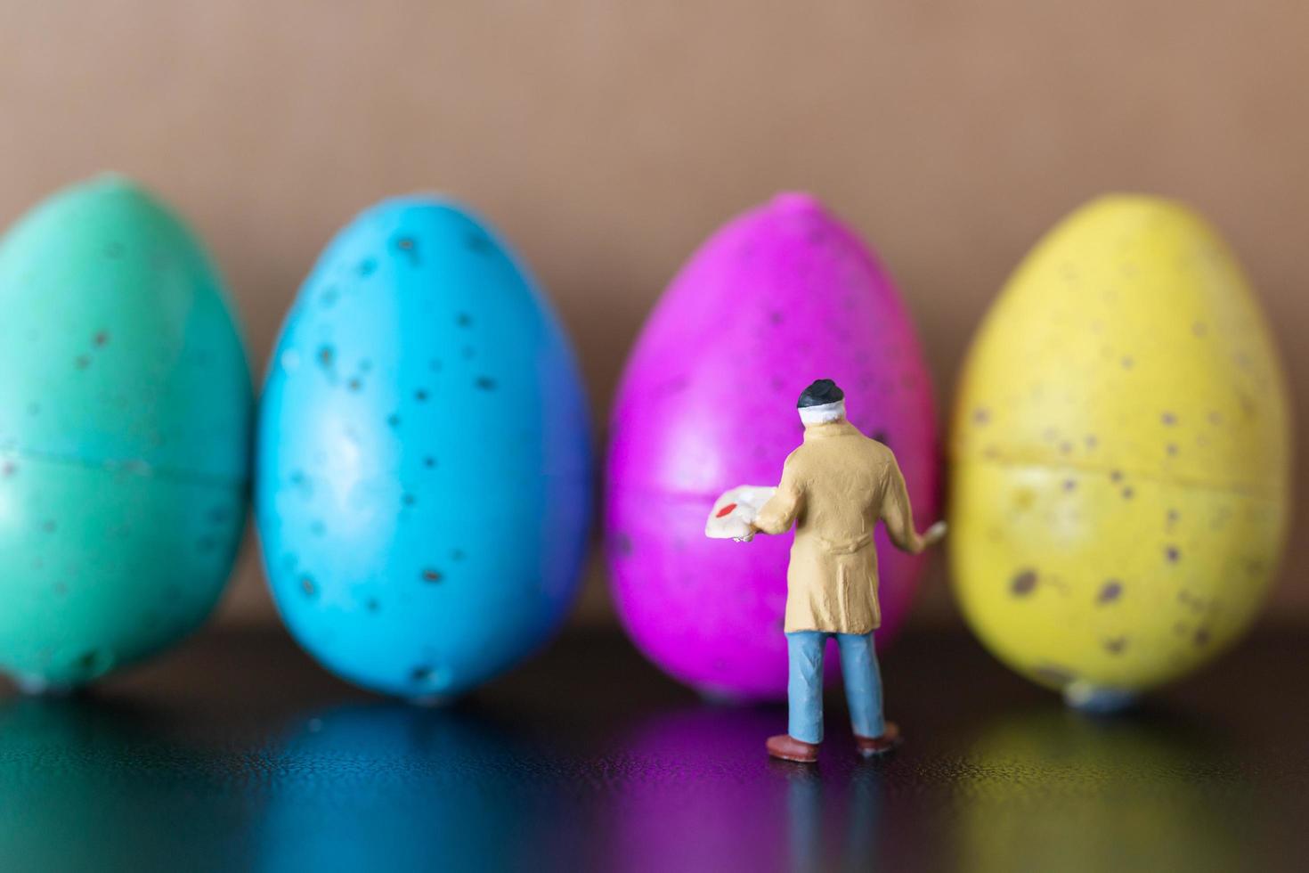 artista in miniatura che tiene un pennello e dipinge le uova di Pasqua per la Pasqua foto