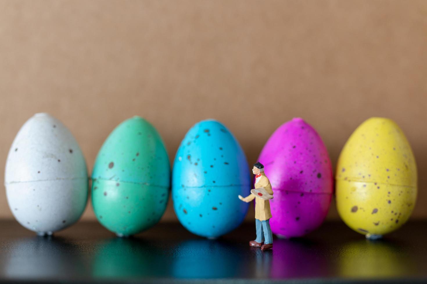 artista in miniatura che tiene un pennello e dipinge le uova di Pasqua per la Pasqua foto