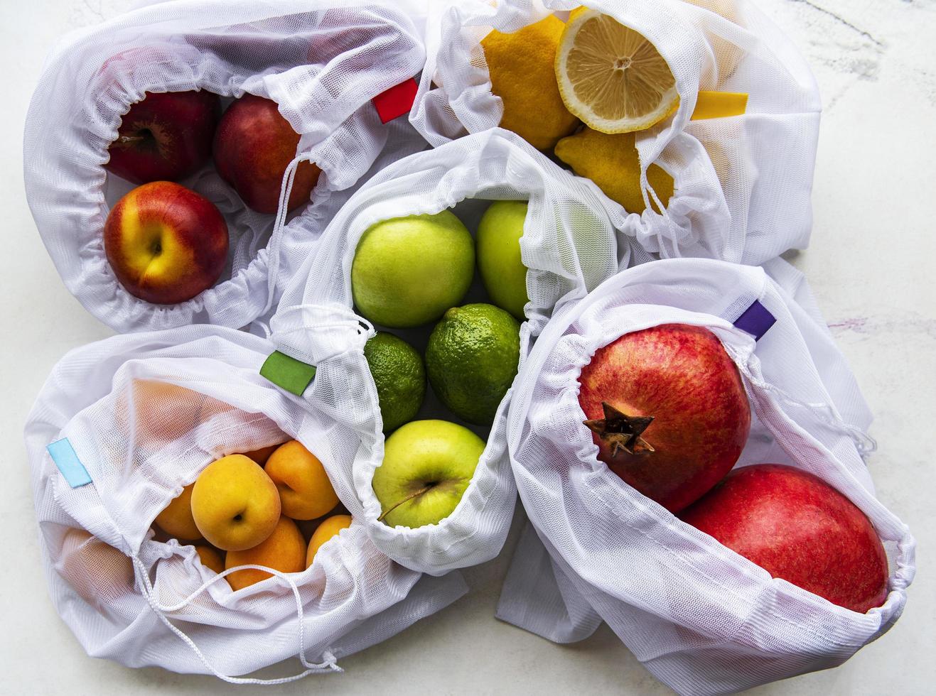 borse della spesa in rete con frutta biologica su fondo in marmo foto