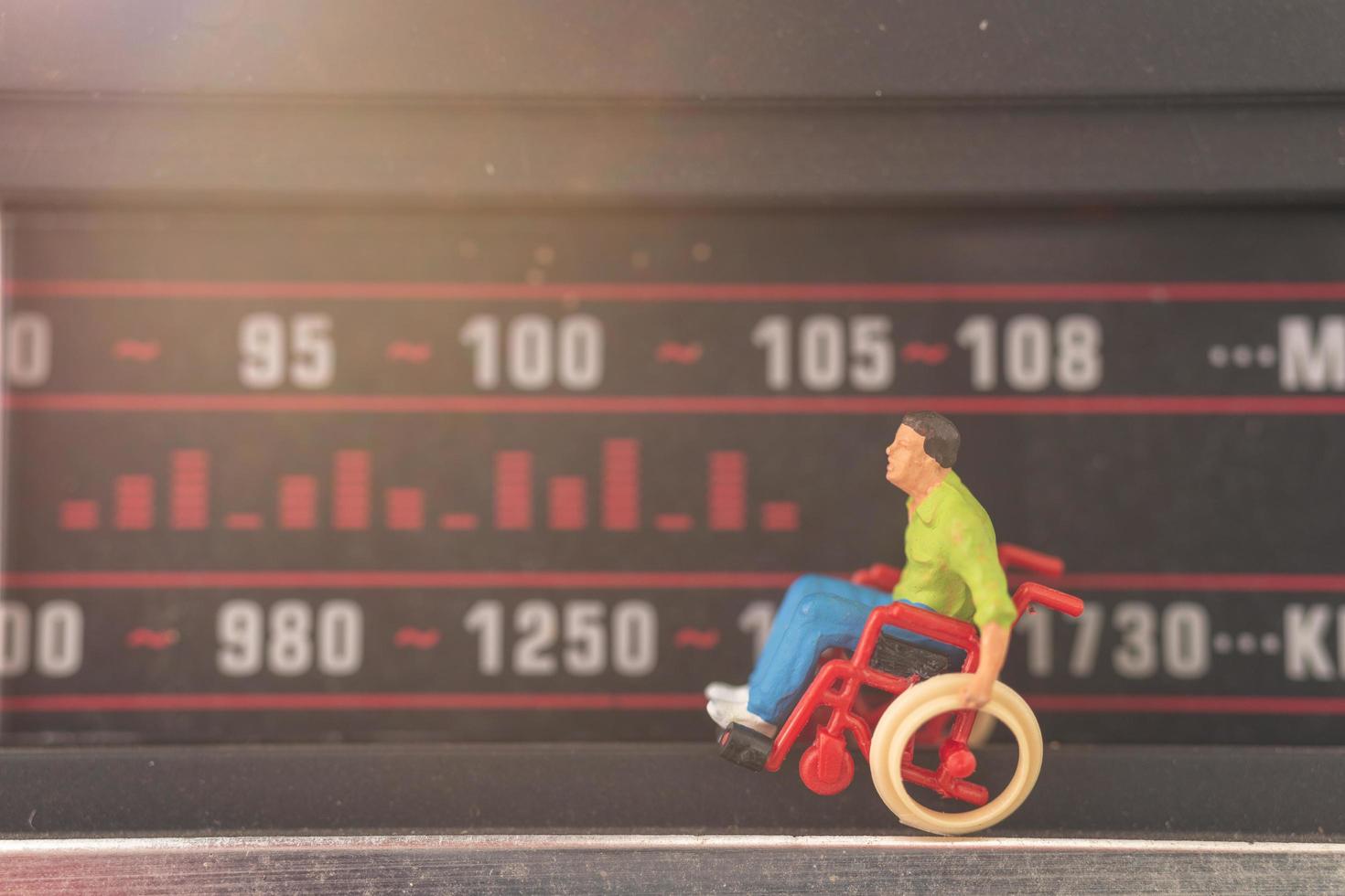 uomo disabile in miniatura seduto su una sedia a rotelle sintonizzarsi su una stazione radio foto