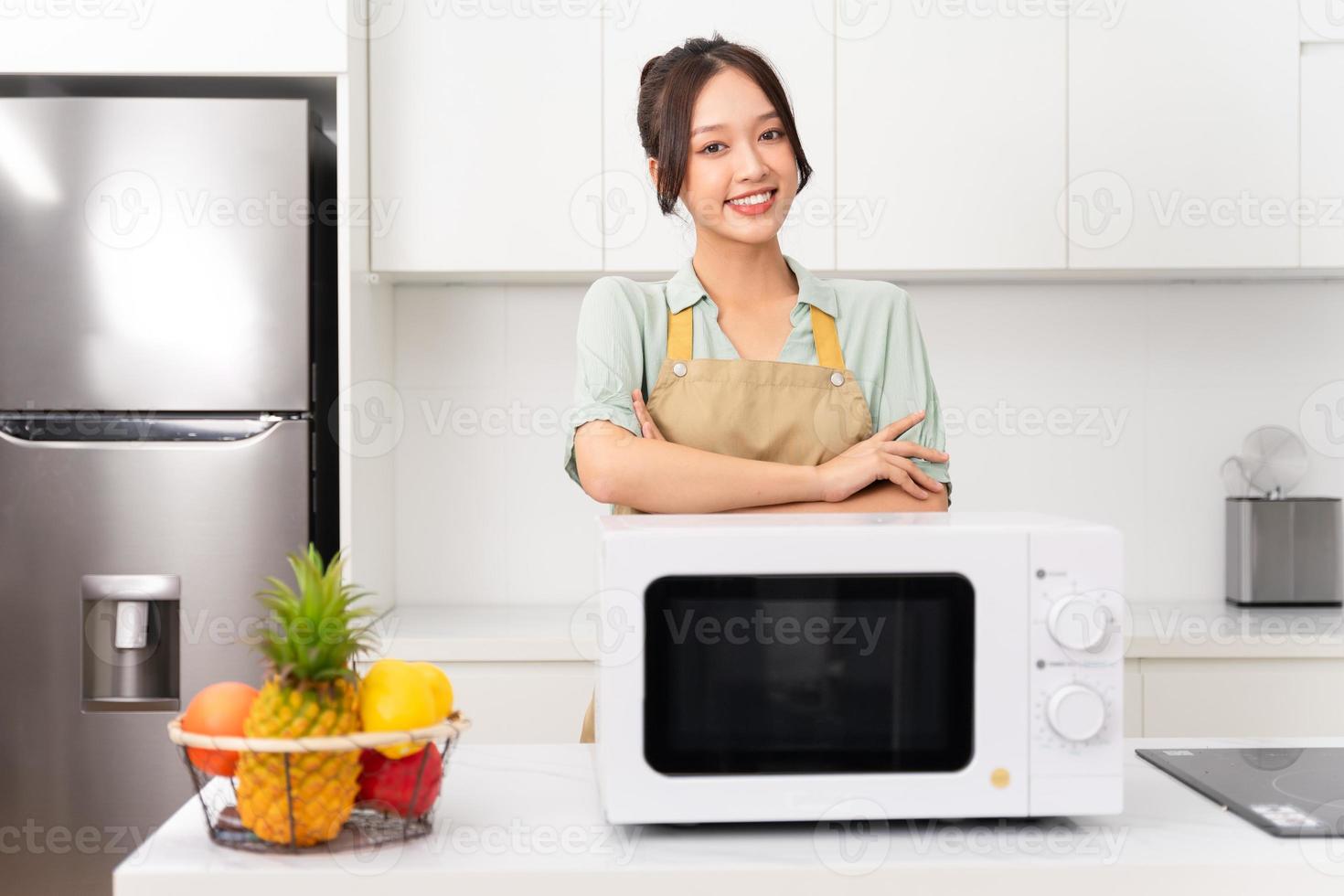 asiatico ragazza in piedi Il prossimo per il microonde nel sua cucina foto