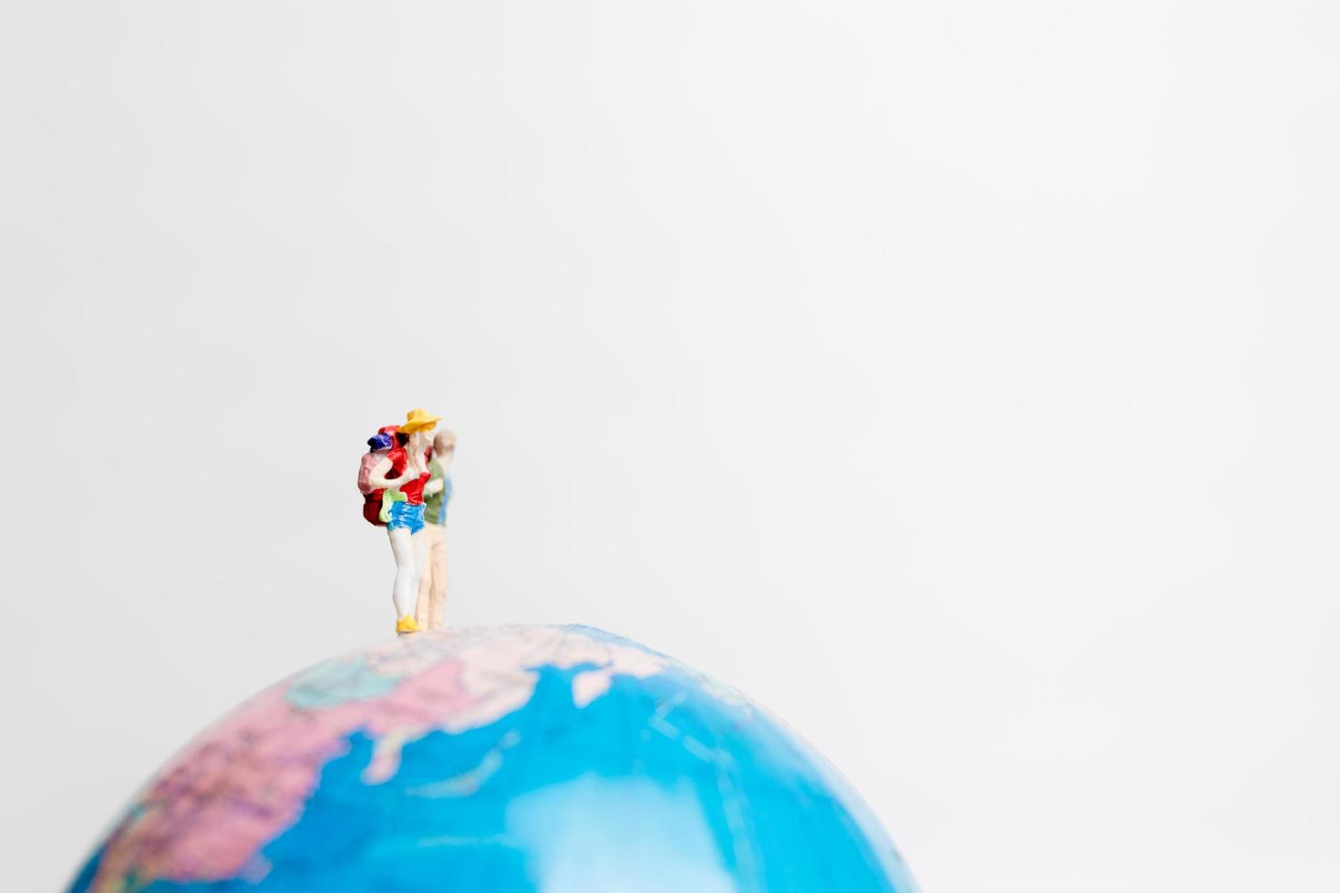 persone in miniatura in piedi su un globo con uno sfondo bianco, concetto di viaggio foto